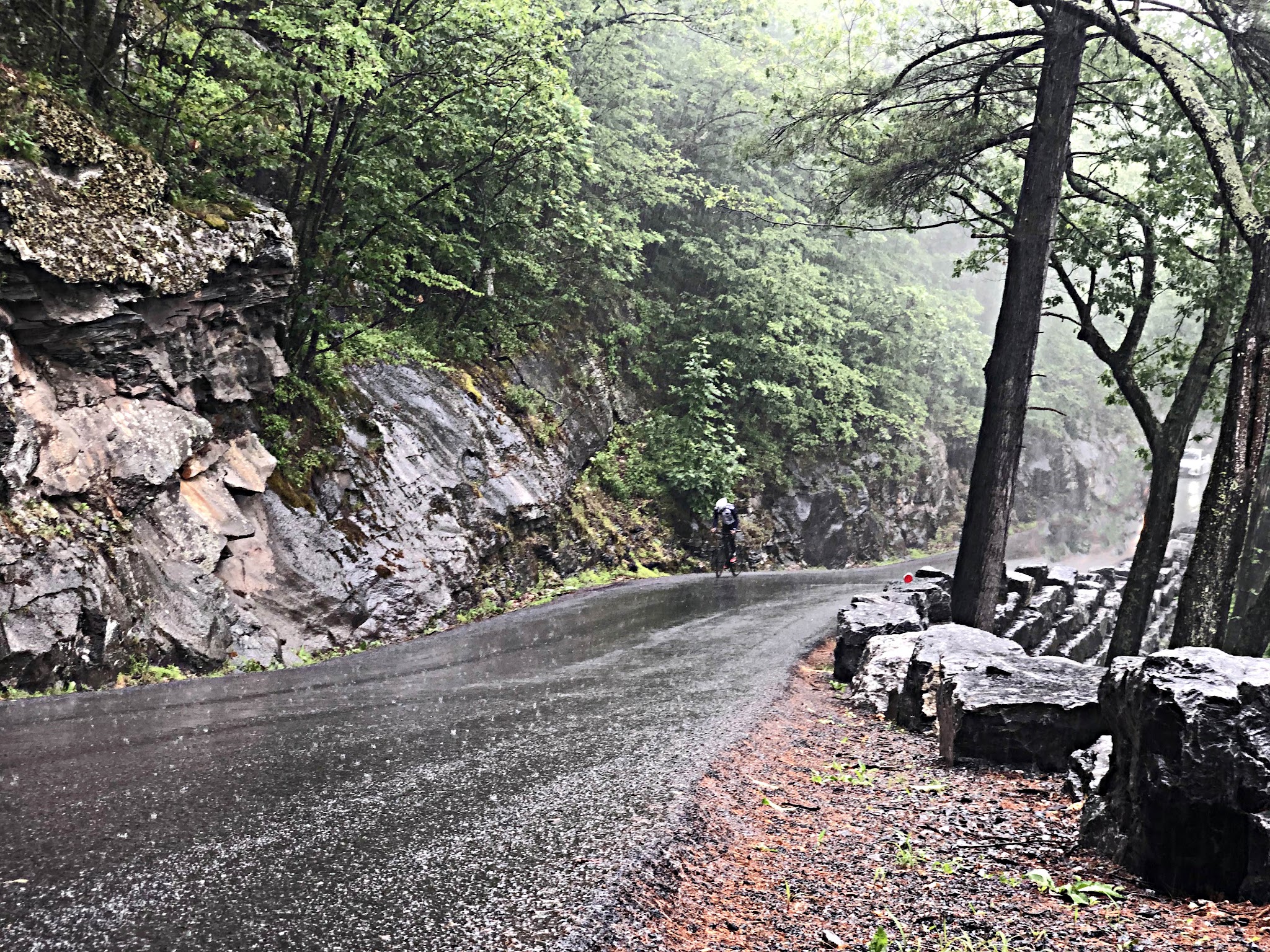 Cycling Devil's Kitchen, Platte Clove Road, New York - cyclist climbing up steep, wet, one-lane roadway surrounded by craggy rock wall on the side, mist and wet greenery 