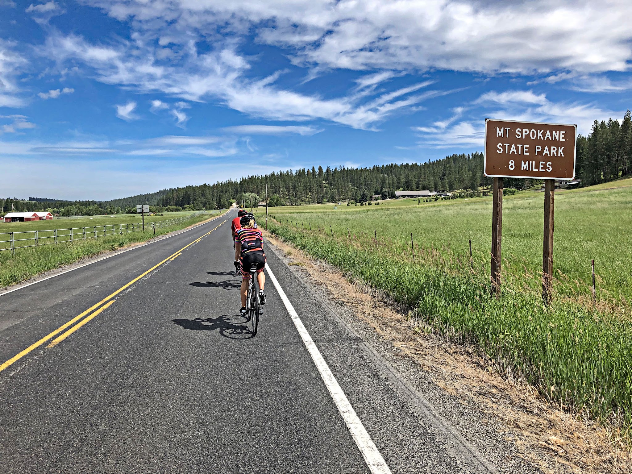 Cycling Mt. Spokane, Washington - cyclists riding single file along two-lane highway, road sign for Mt. Spokane State Park, 8 Miles