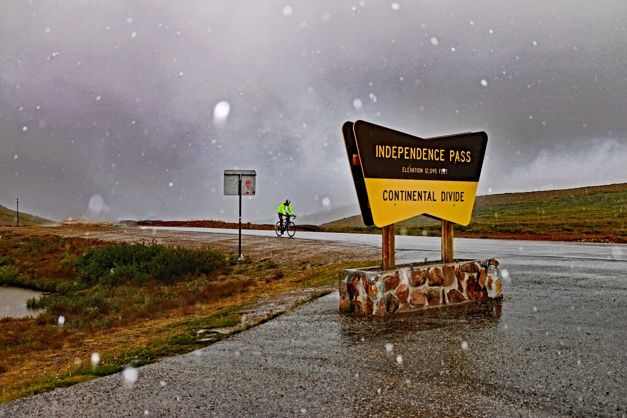 Bicycle ride up Independence Pass - Continental Divide sign and cyclist riding to it. 