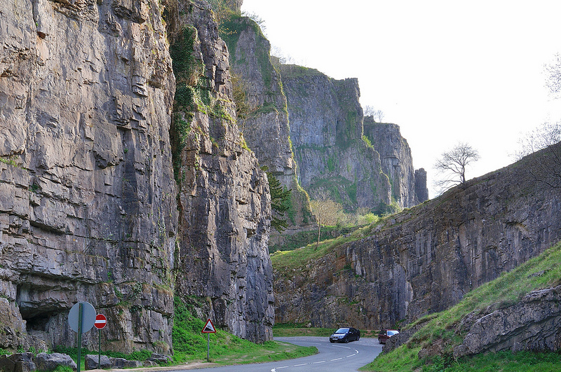 Cycling Cheddar Gorge - tall limestone rock walls with green grass growing atop sloped portions, road in center