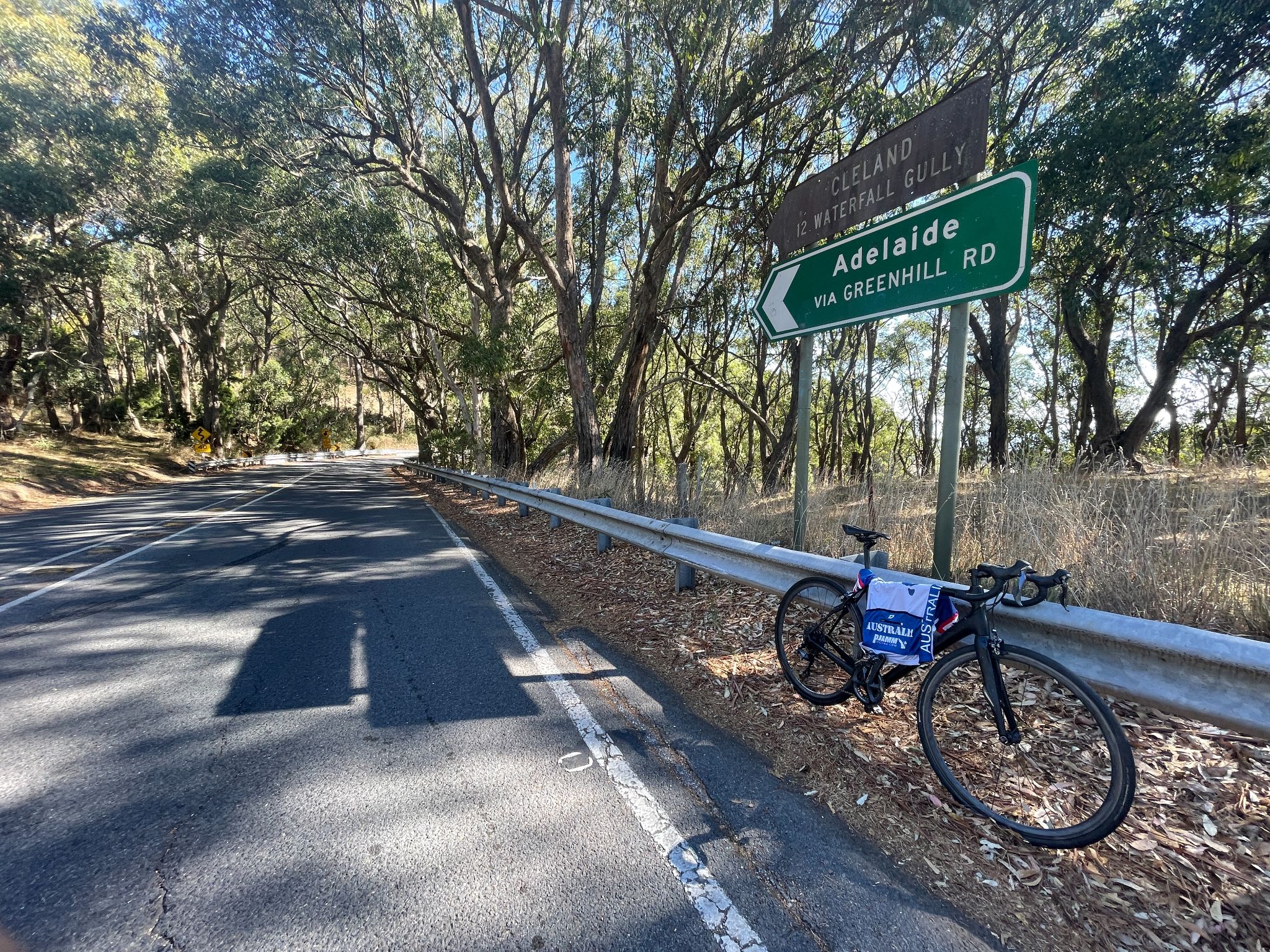 bike parked against guardrail in front of road sign for Adelaide via Greenhill Road