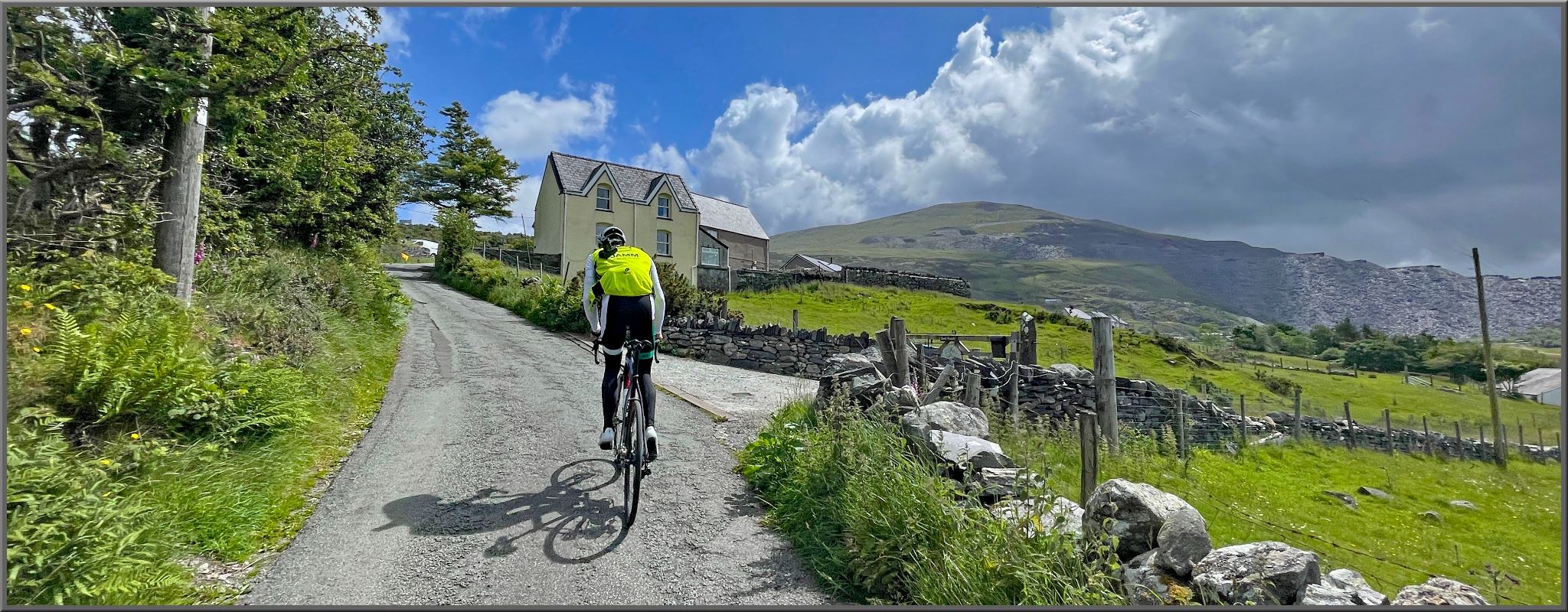 PJAMM Cyclist rides up narrow one-lane roadway, large white country house in distance