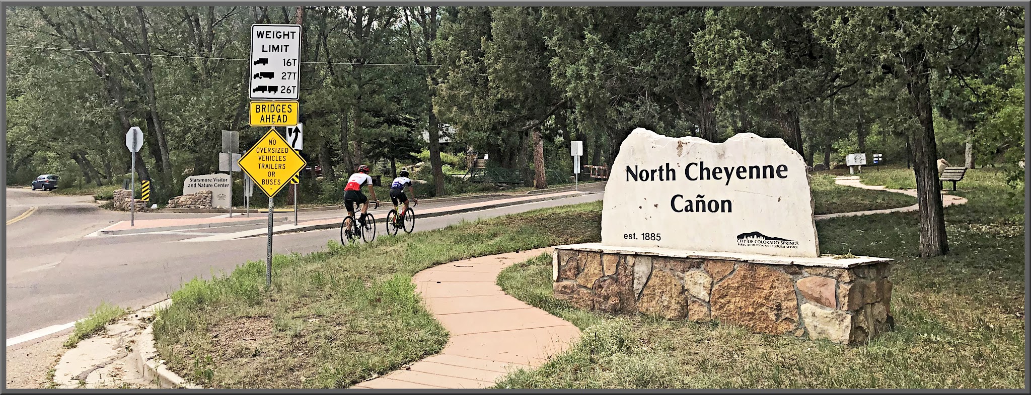 Cycling North Cheyenne Cañon, Colorado Springs - two cyclists on roadway near stone sign for North Cheyenne Cañon