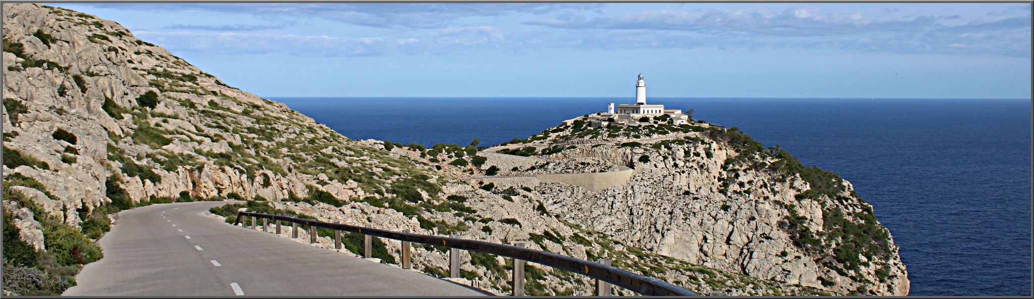 panoramic view of two-lane highway roadway leading to white lighthouse, blue ocean surrounding roadway