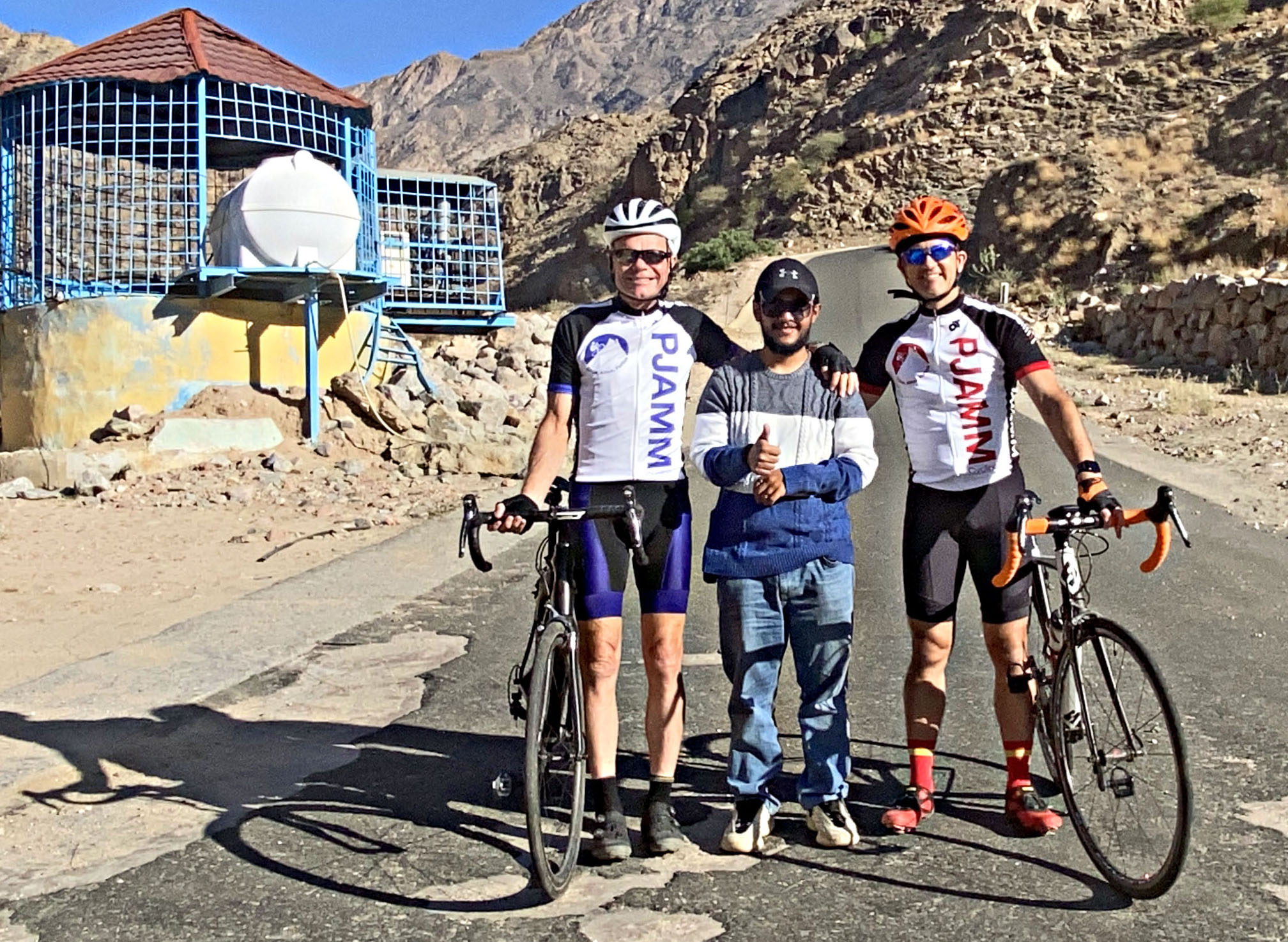 Asir Mountains, Saudi Arabia Asir Mountains, Saudi Arabia - PJAMM Cyclists stand with bikes in center of the roadway, with guide Adnan smiling and giving a thumbs up between them.