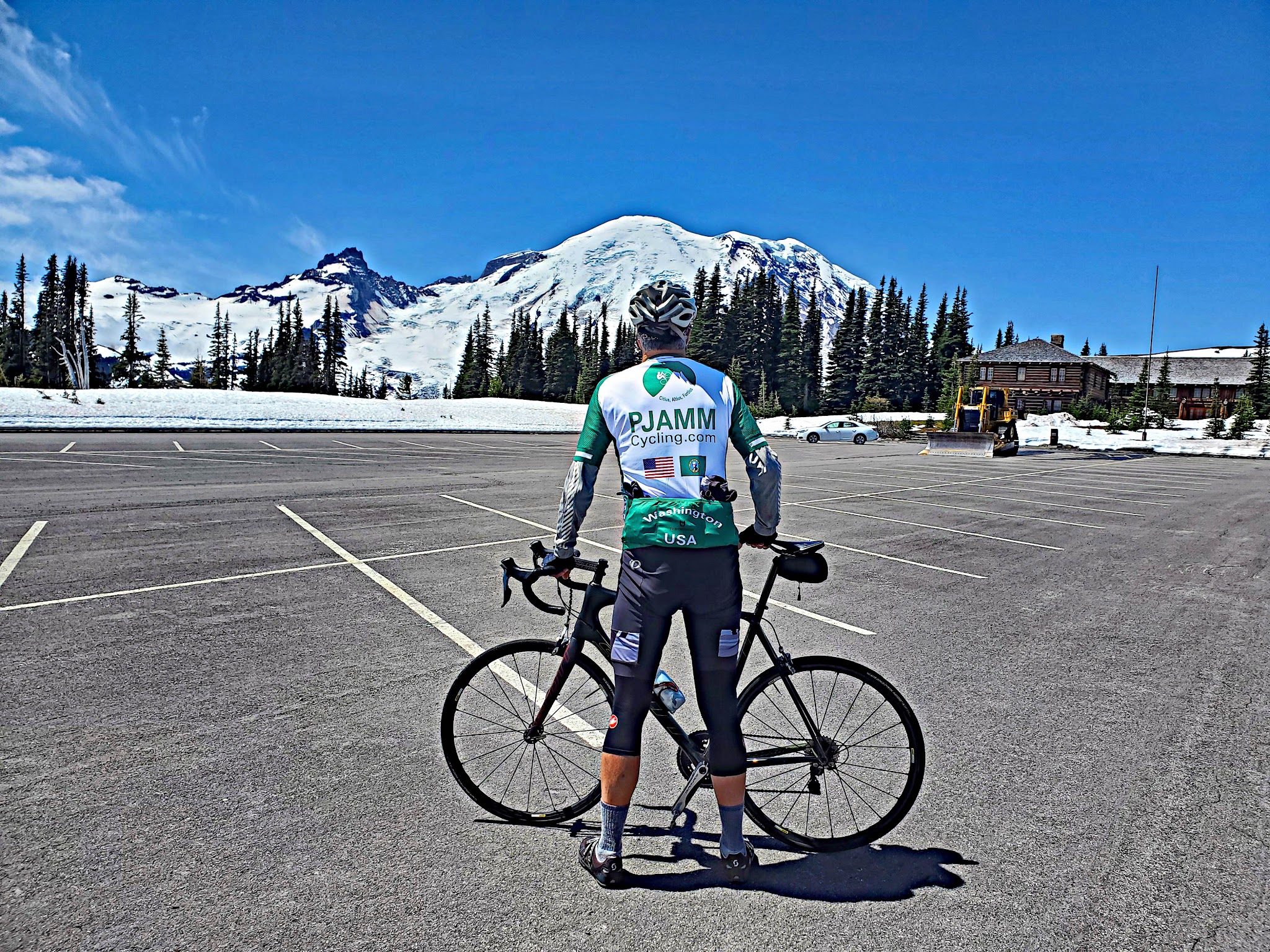 Cycling Mt. Rainier, Sunrise VC, Washington - cyclist standing in parking lot with bike, facing snow covered Mt. Rainier, wearing PJAMM Cycling jersey