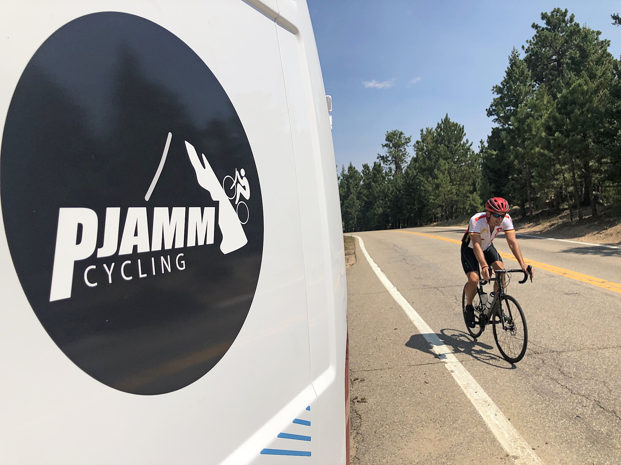 Cycling Flagstaff Road, Boulder, Colorado - close up of decal on PJAMM Cycling SAG vehicle, cyclist riding on roadway next to van