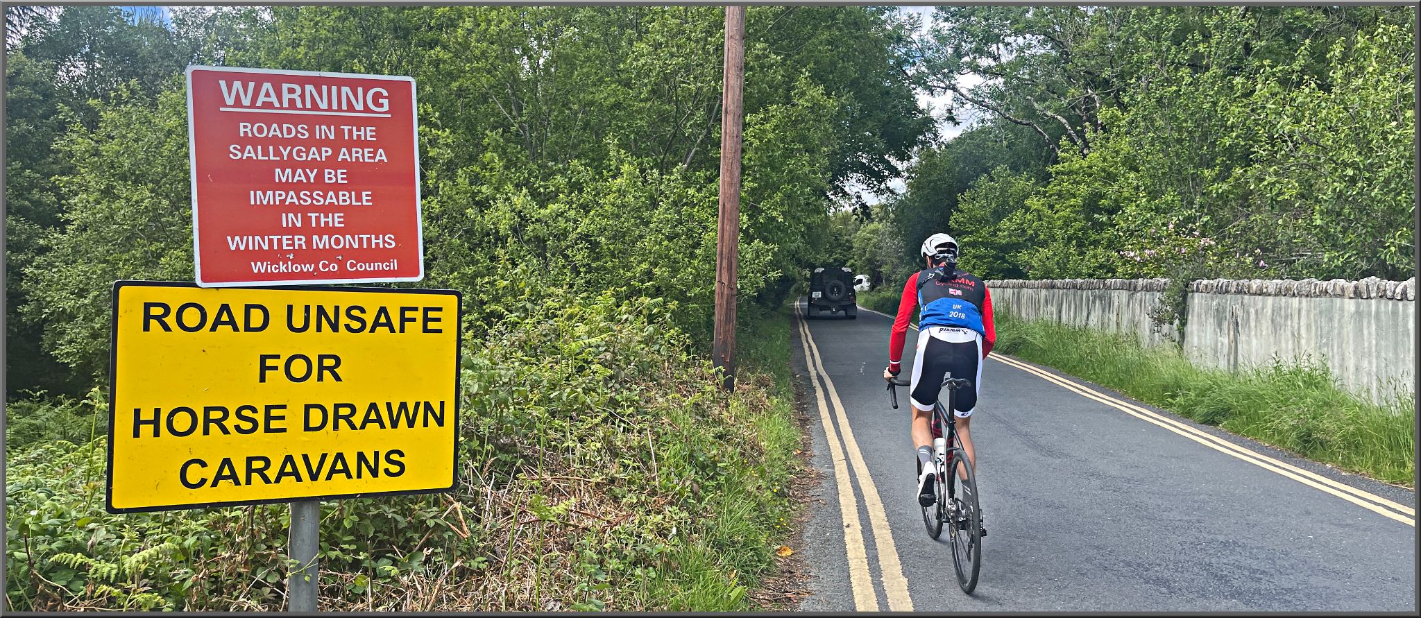 PJAMM Cyclist rides past street signs reading "Warning roads in the Sallygap area may be impassable in the winter months," and "Road unsafe for horse drawn caravans"