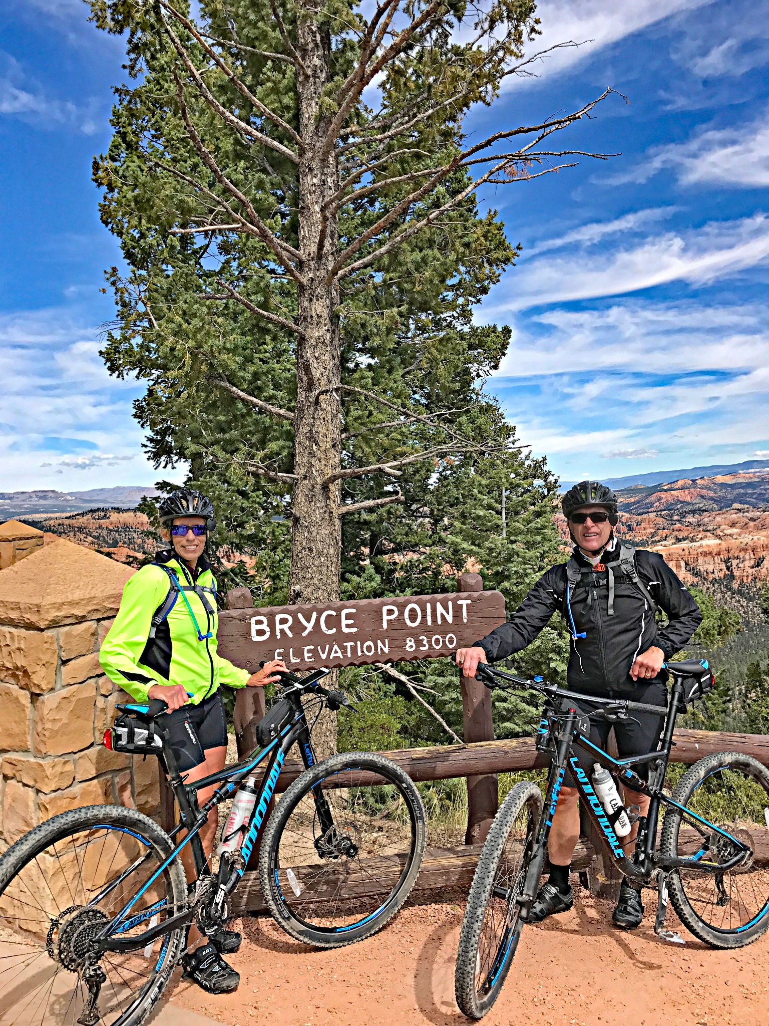 Cycling Bryce Canyon National Park, Utah - two cyclists stand on red dirt path in front of sign for Bryce Point