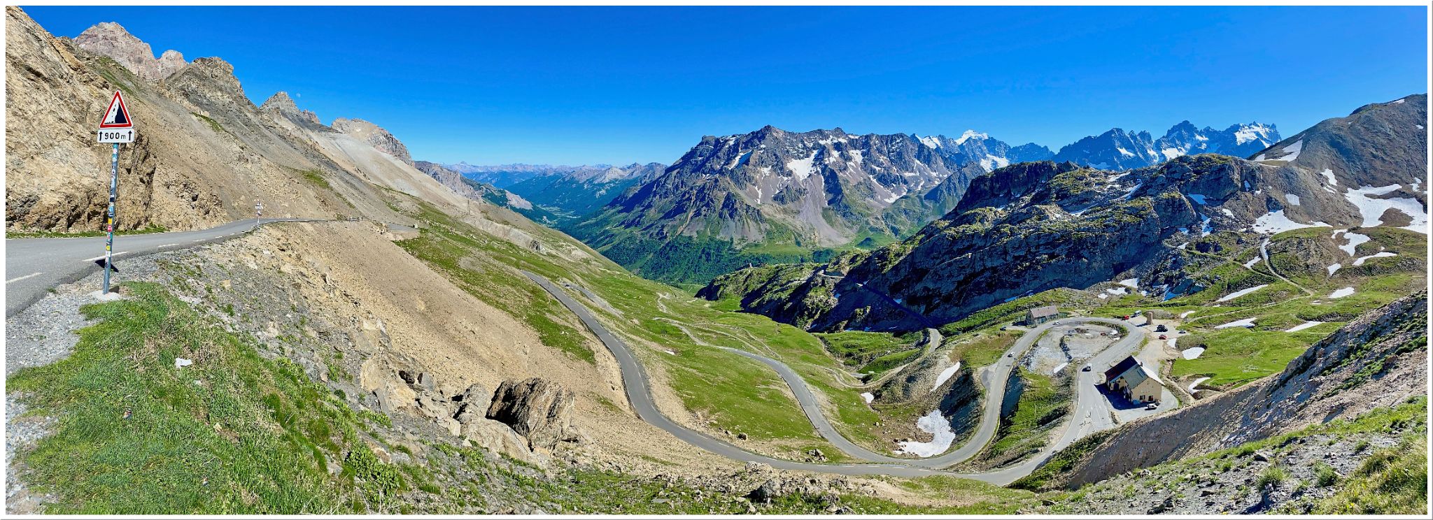 panoramic view shows road winding through hills and valley below, snow-capped mountains in background