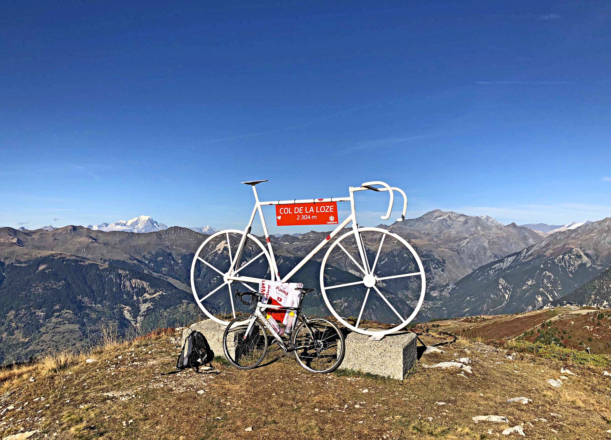 large white bike statue at climb's finish, with red sign reading Col de la Loze; alpine vista views in background