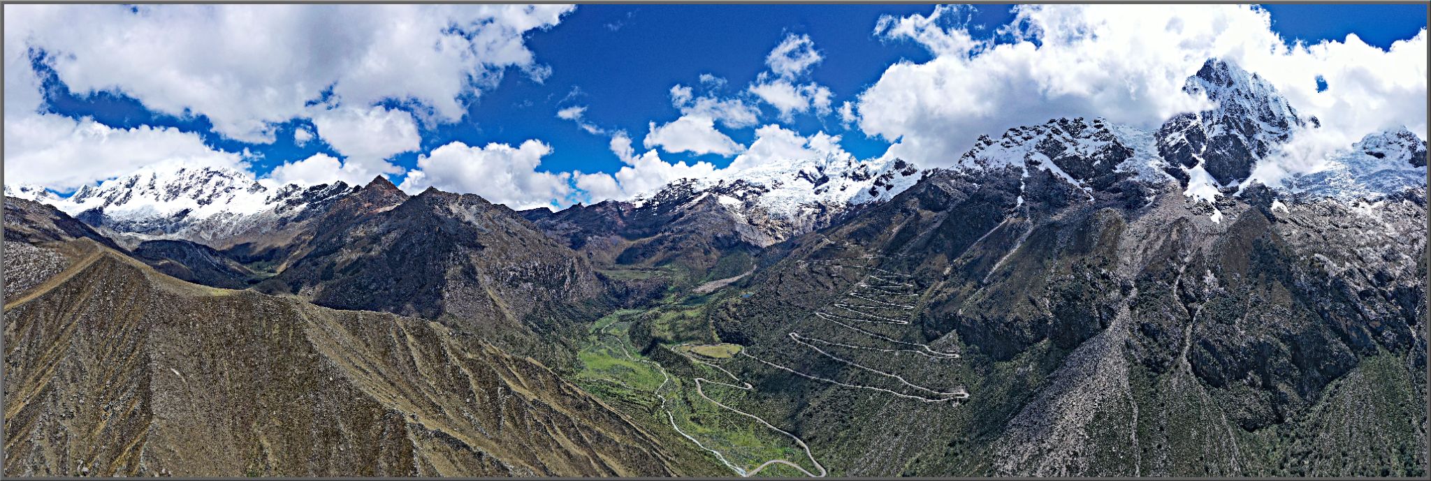 Panoramic views of mountain peaks covered in snow, sharp mountain road snaking up mountainside