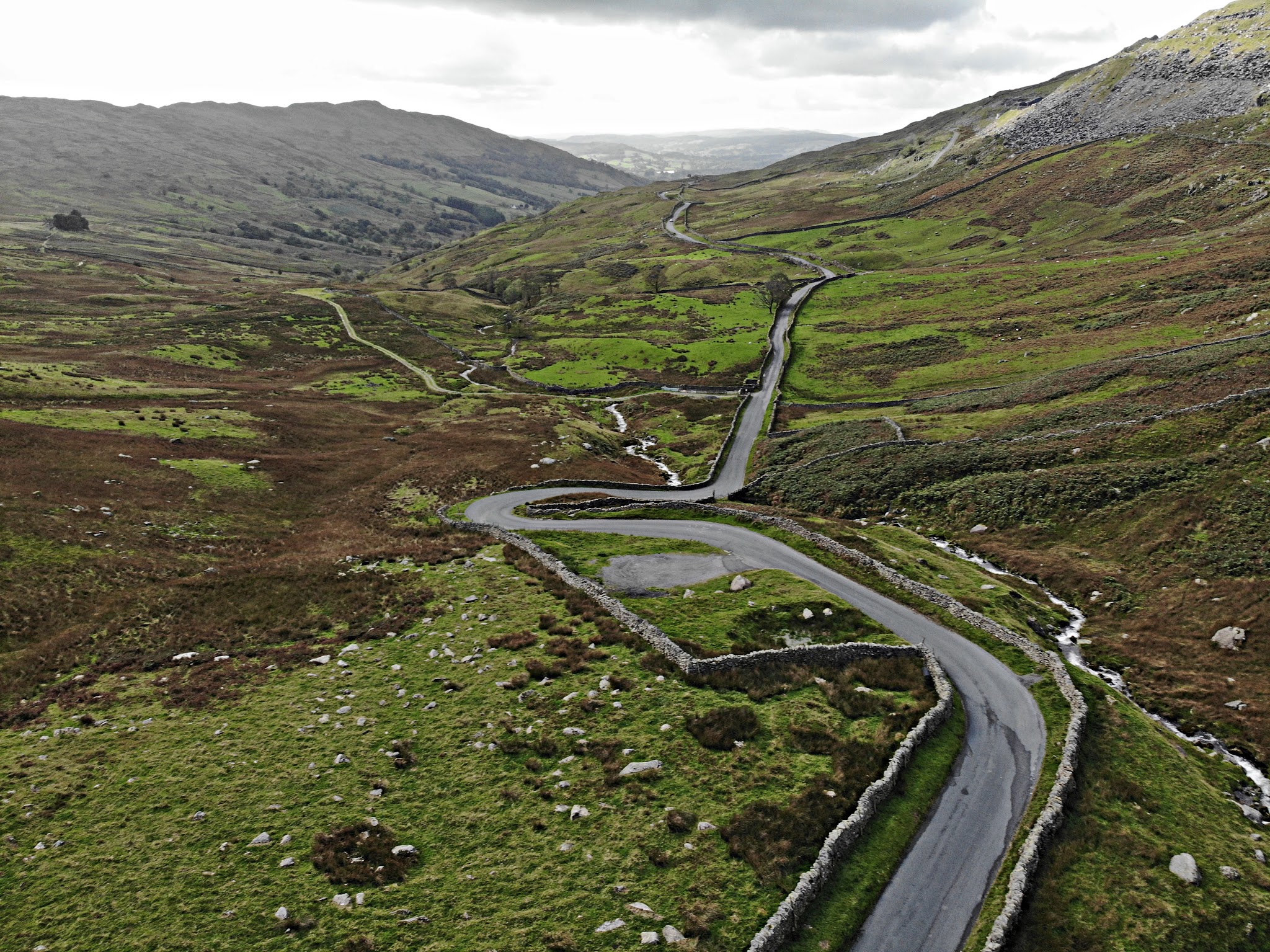 Cycling Kirkstone from Ambleside (The Struggle) - aerial view of one-lane, stone wall lined road winding through countryside hills, sheep grazing in pastures 
