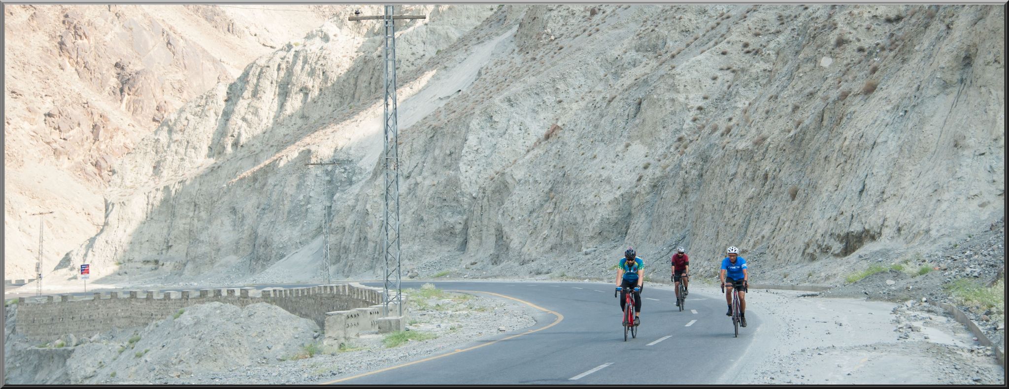 Chilas to Babusar, Pakistan - Three cyclists ride on two lane roadway in high desert landscape