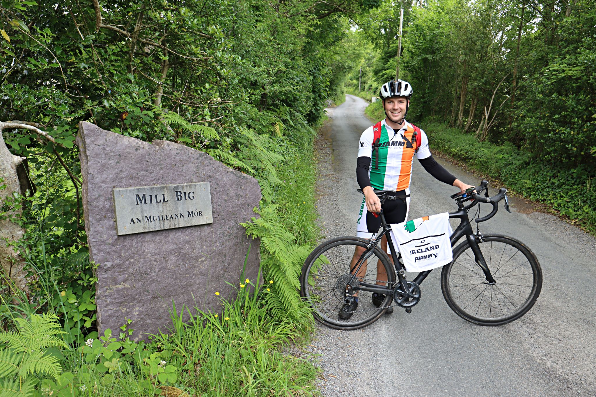 PJAMM Cyclist Brad Butterfield stands with bike next to stone sign reading "Mill Big"