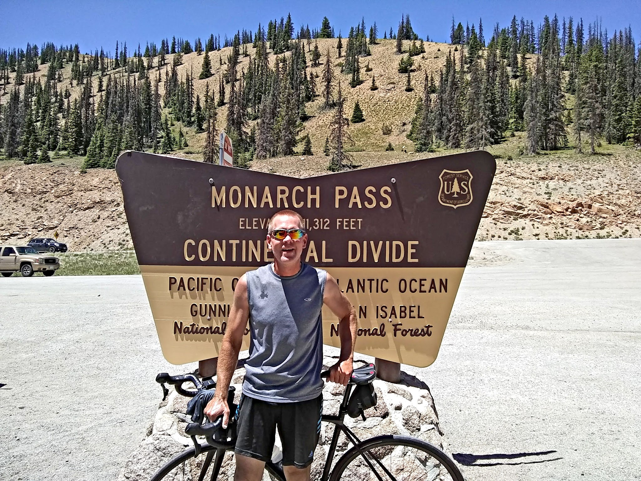 Cycling Monarch Pass East, Colorado - Cyclist Chris Jacobs standing with bike in front of NPS Monarch Pass Continental Divide sign