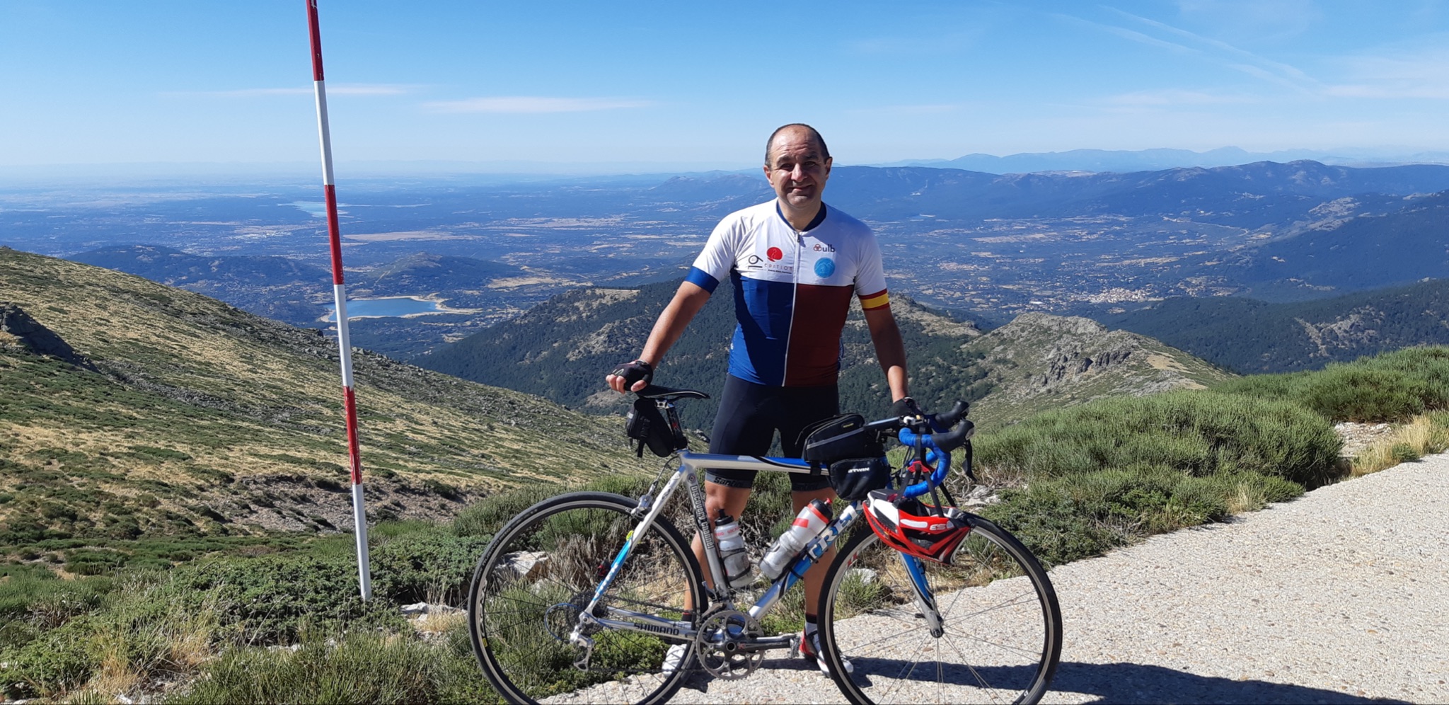Cycling Bola del Mundo vía Puerto Navacerrada, Spain - cyclist stands with bike at climb summit, panoramic views beyond