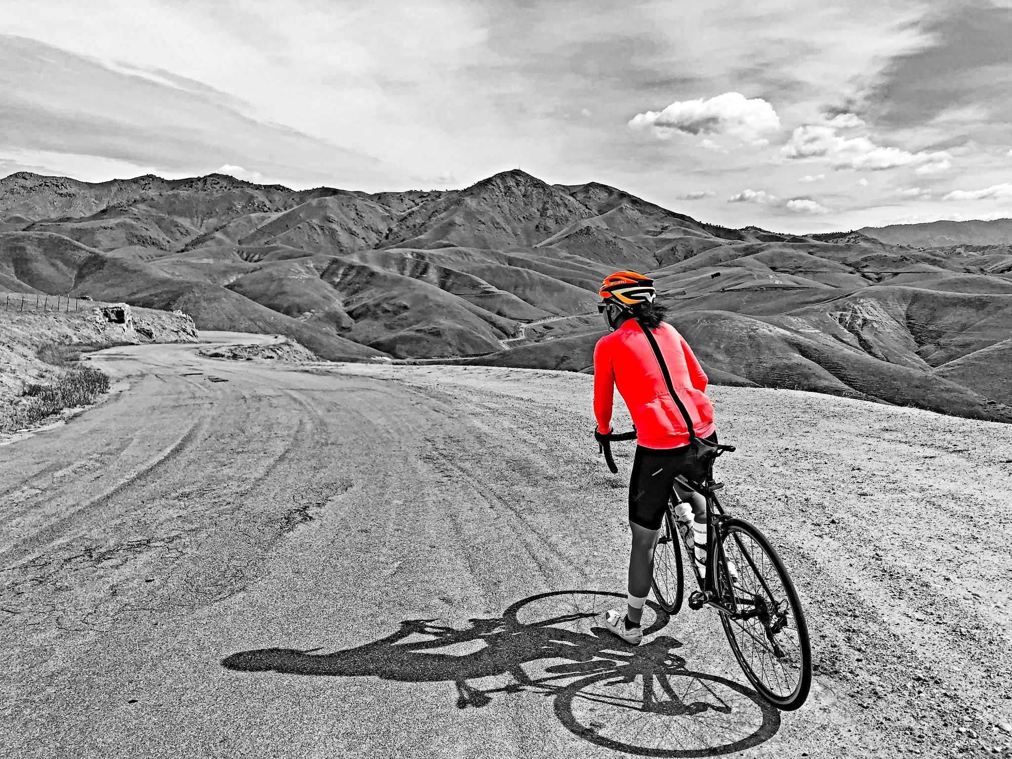Cycling Breckenridge West, California Cycling Breckenridge West, California - cyclist on bike in center of wide winding roadway, mountains in distance. all of photo is black and white except for cyclist's red jersey and red helmet