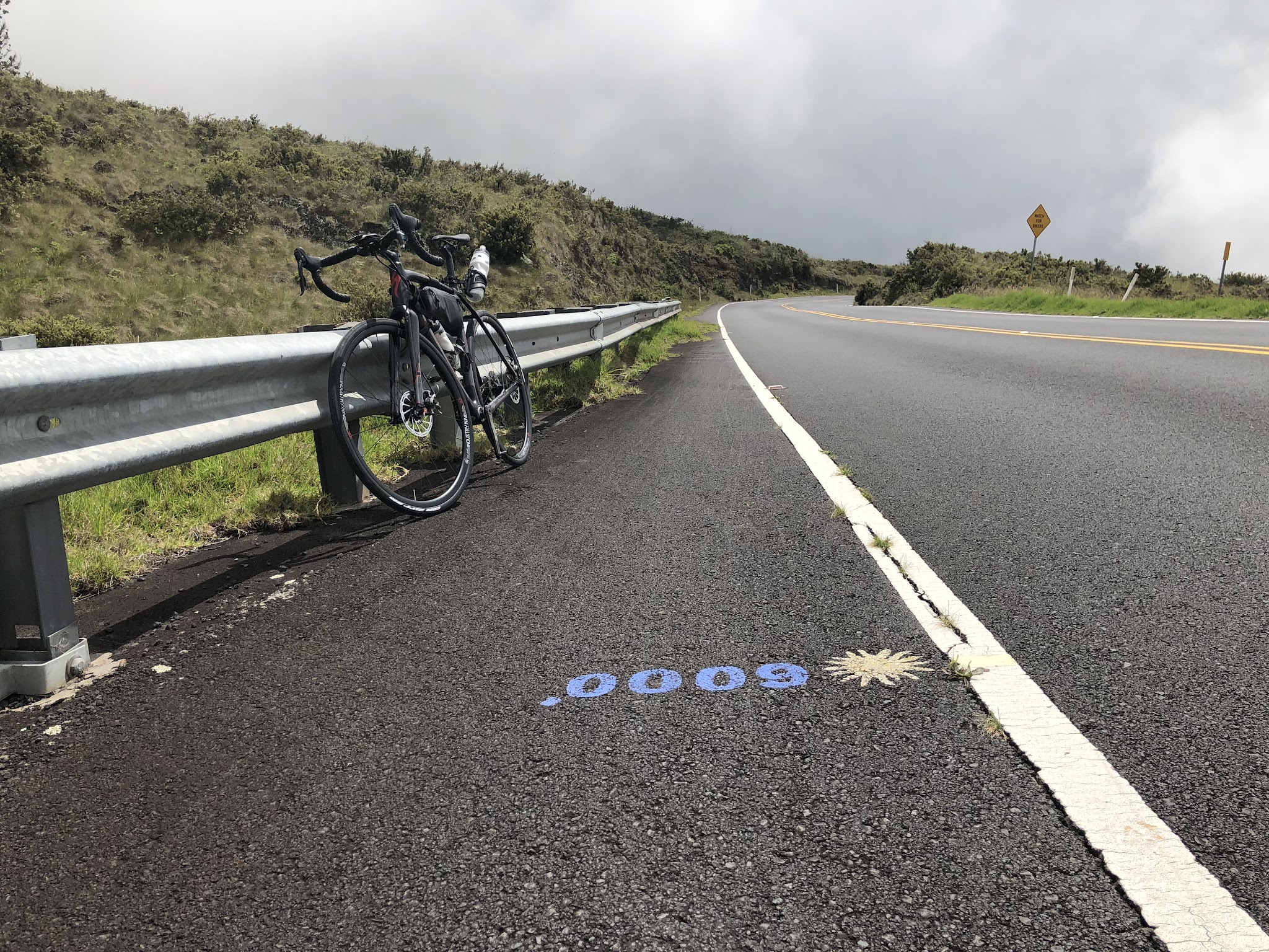 Climbing Haleakala Volcano  by bike - road altitude markers, roadway, clouds and bike