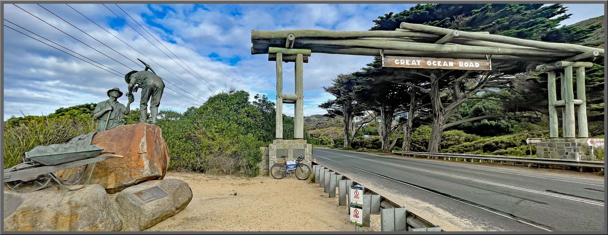 sign hangs over road reading "Great Ocean Road," statue of two miners on road side
