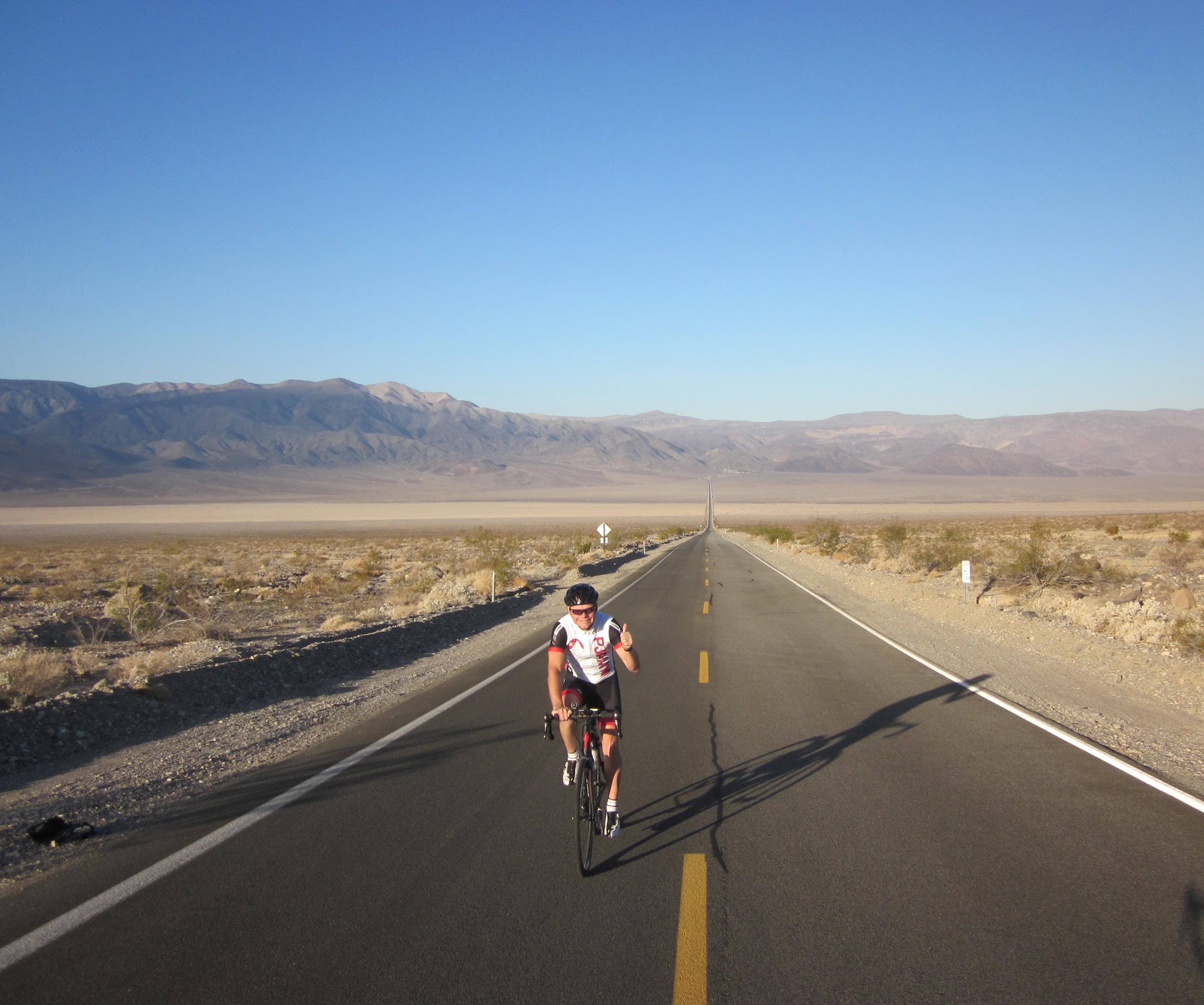 Cycling Death Valley National Park, California Cycling Death Valley National Park, California - PJAMM Cyclist John Johnson rides on long, straight, two-lane highway road through desert landscape