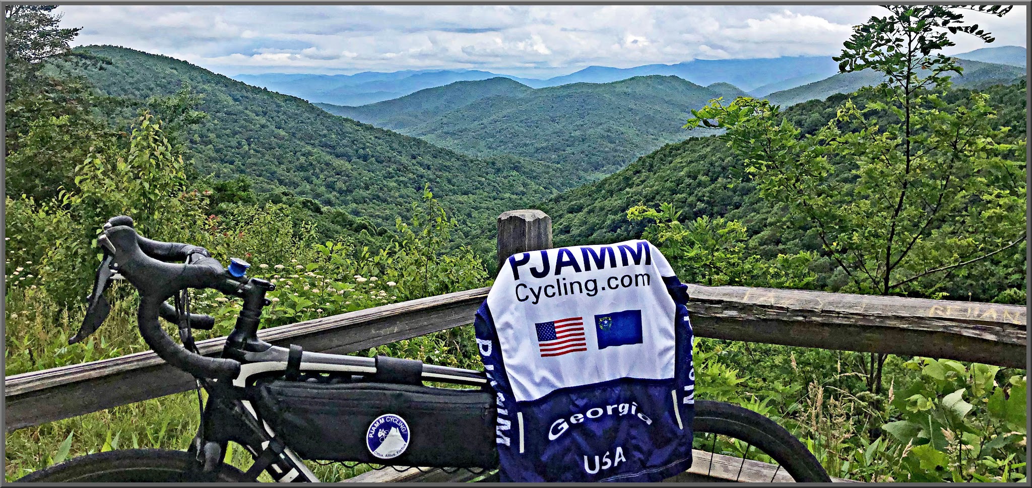 Cycling Hogpen Gap West - road bike with PJAMM Cycling jersey laid out over seat, bike leaning against wooden railing, overlooking lush green ridge lines and mountainside with wildflowers