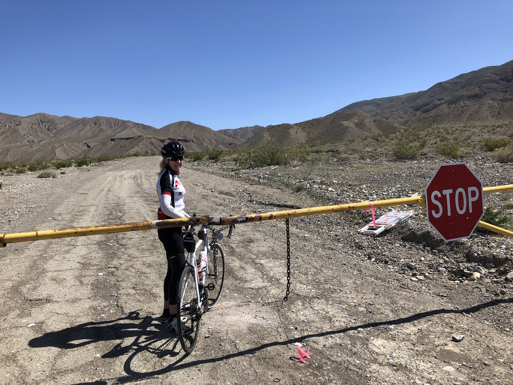 Cycling Death Valley National Park, California - cyclist stands with bike beyond closed gate at Wildrose