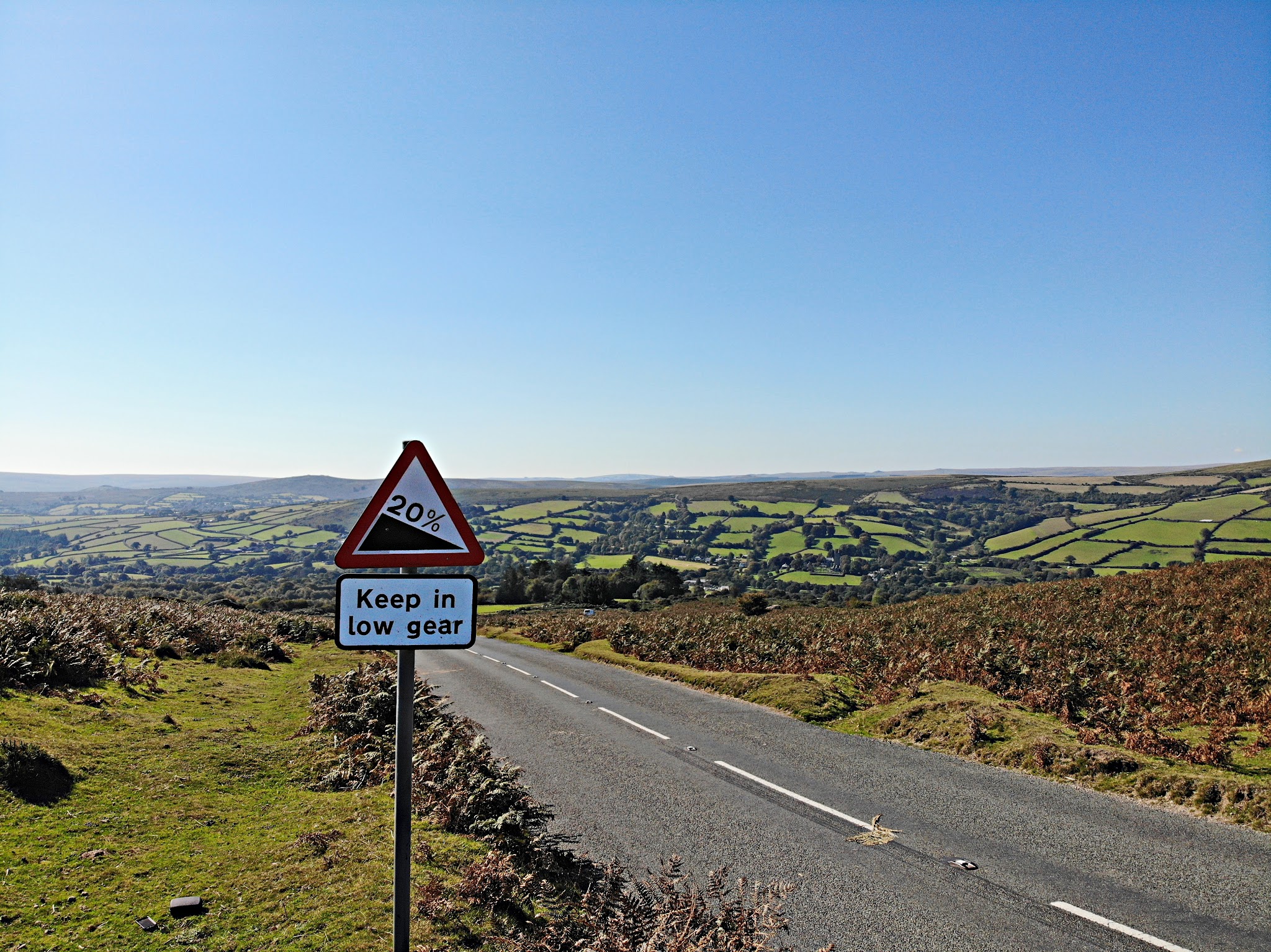 Cycling Widecombe - view from top of climb looking back down over pastureland, straight, two-lane road, road sign for 20% grade
