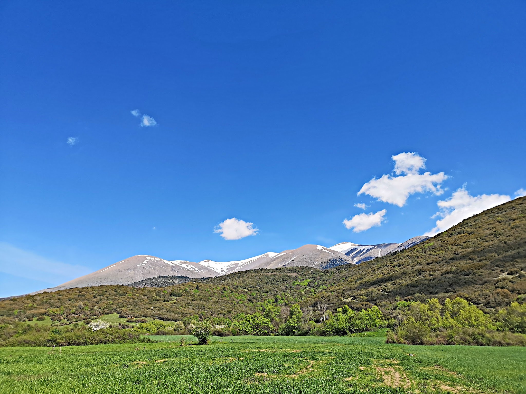 Cycling Mount Olympus, Greece - view from green grassy field looking out toward mountains, blue sky and white clouds beyond