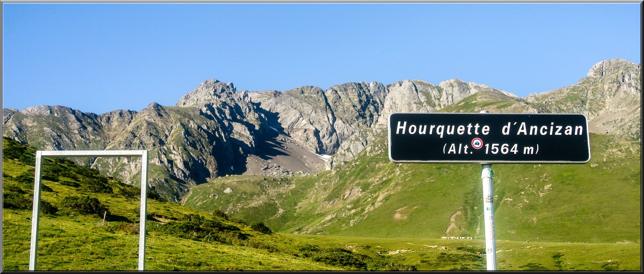 road sign for Hourquette d'Ancizan in front of bright green hillside and sharp stone mountain faces