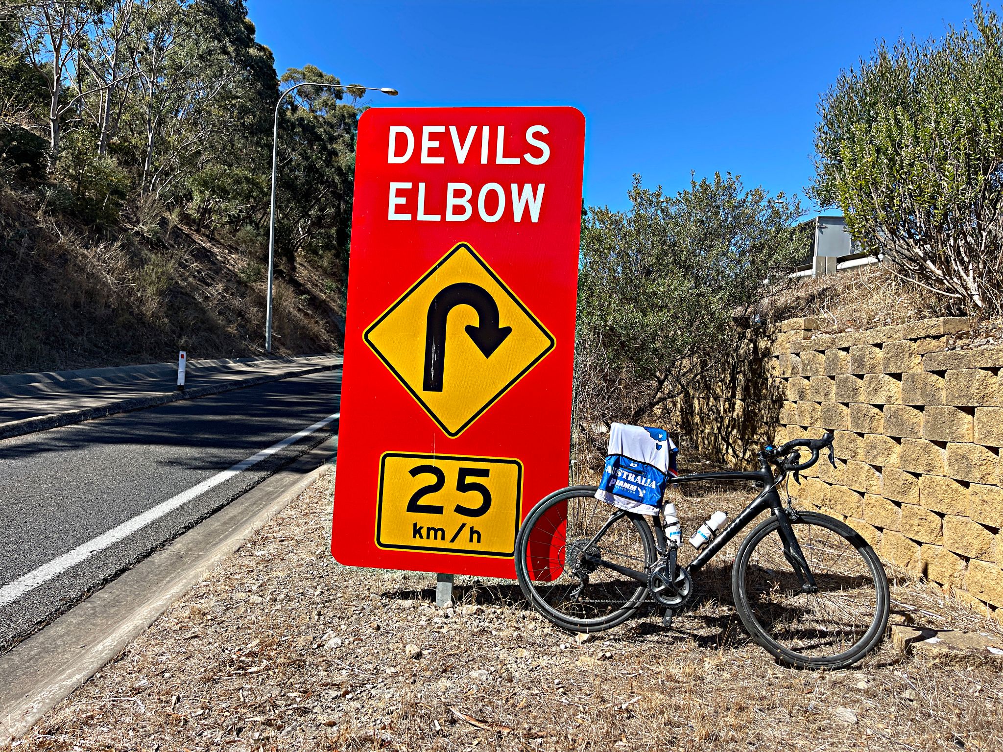 bike and jersey leaning against large red and yellow road sign for Devils Elbow