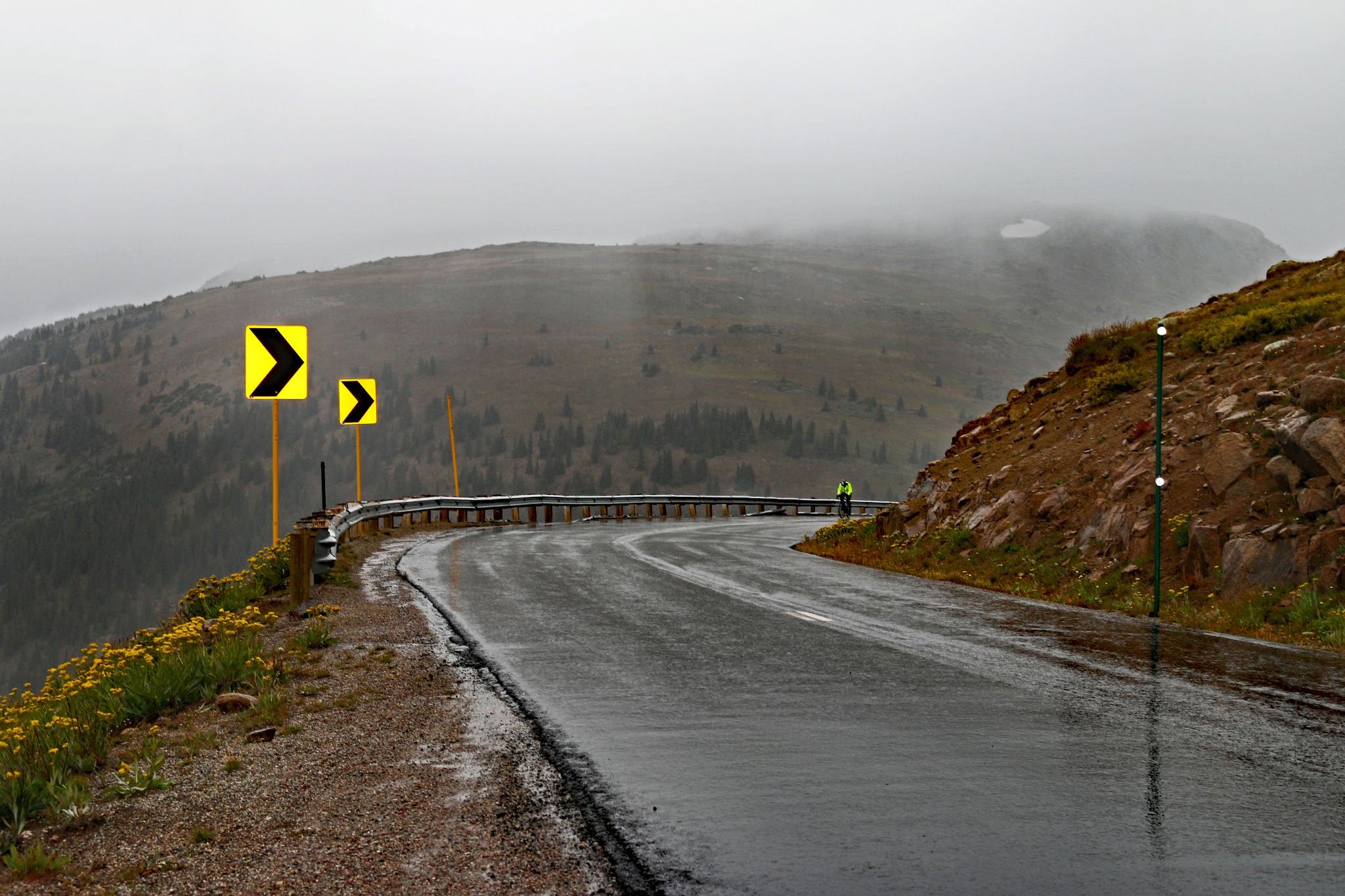 Bicycle climb of Independence Pass - cyclist riding up roadway in rain.