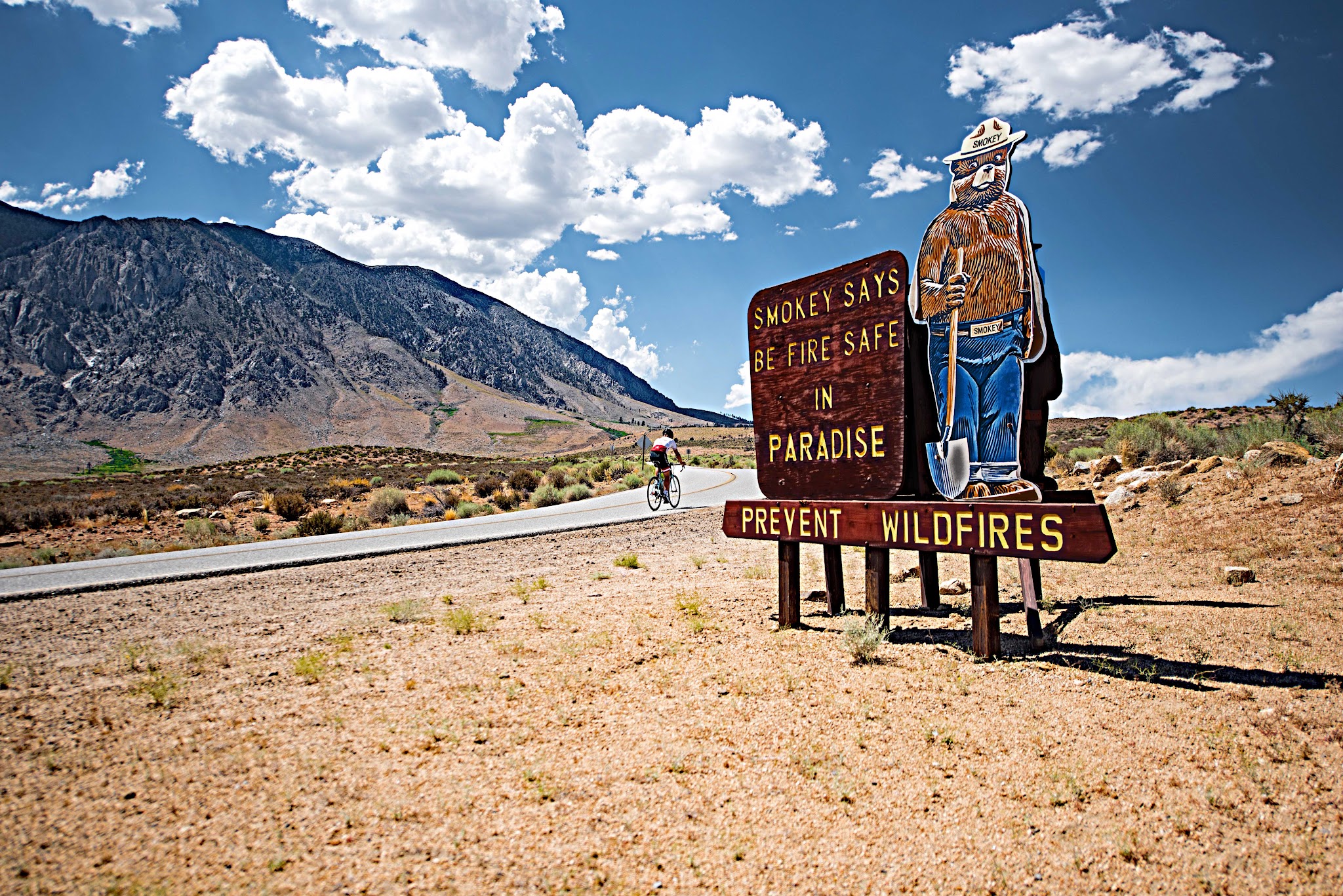 Bicyclist passing Smoky the Bear sign on Rock Creek Road Inyo County