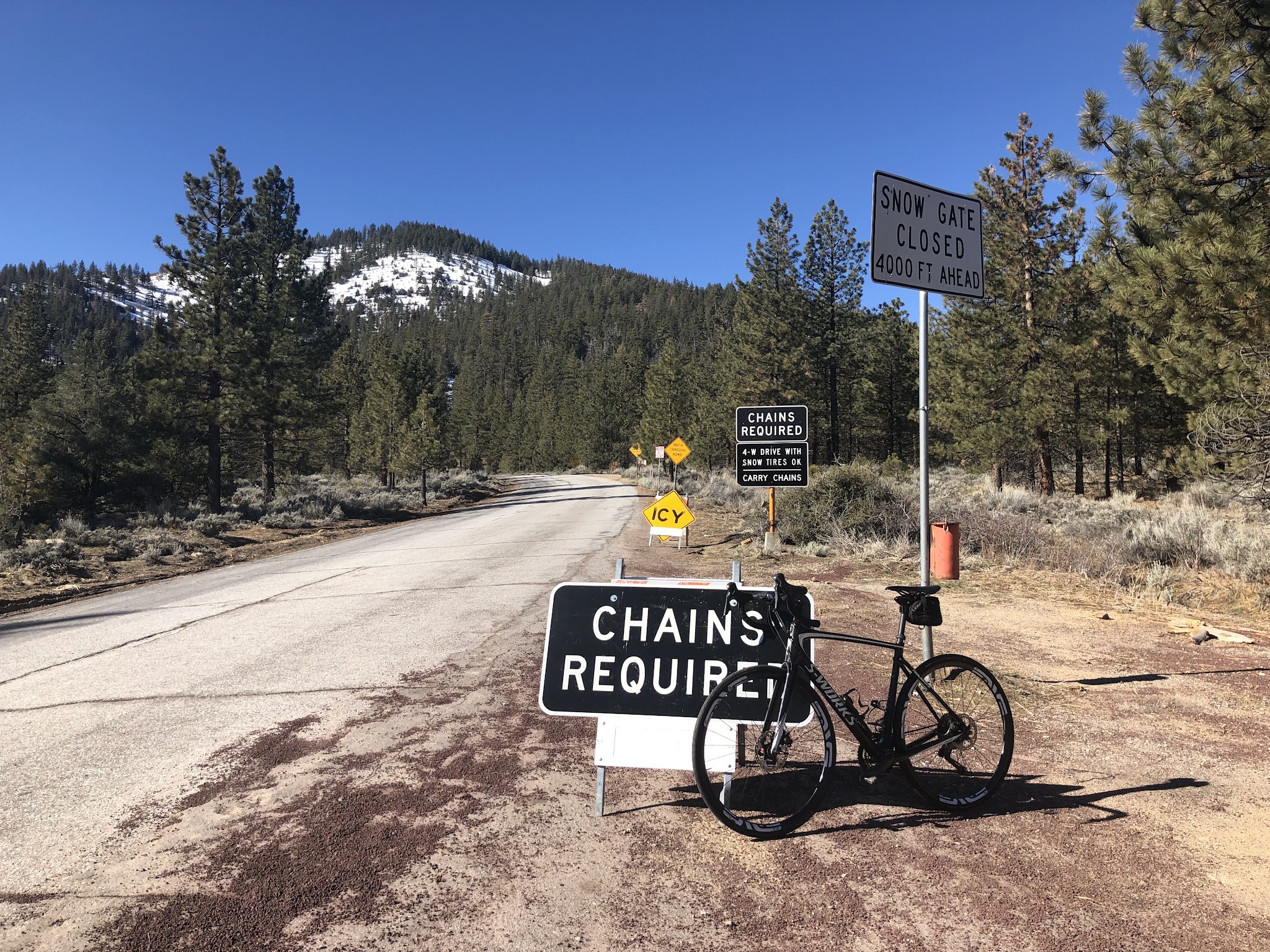 Climbing by bike Mt. Pinos - bike leaning against chains required sign, road, snow covered mountain