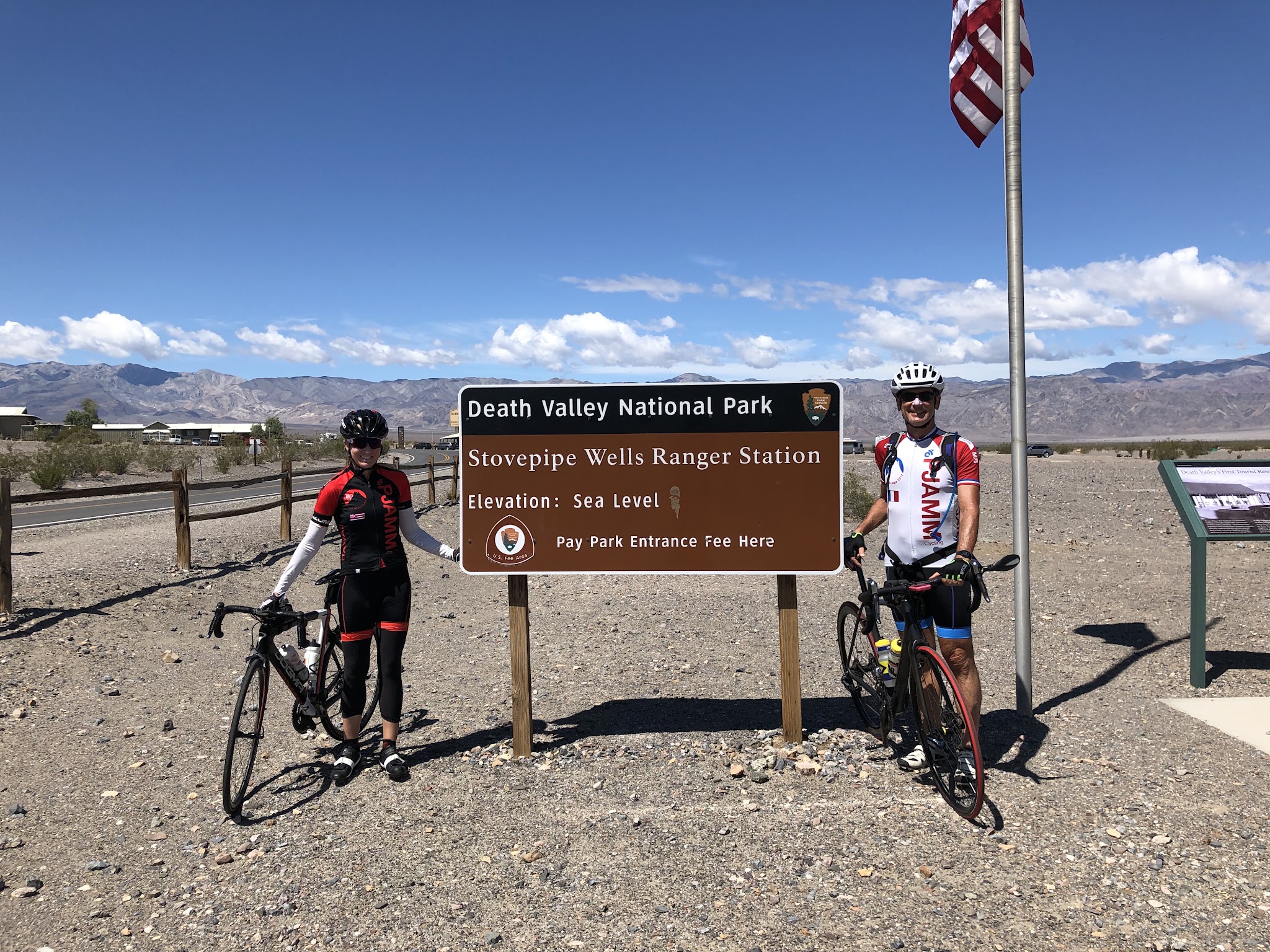 Cycling Death Valley National Park, California - two PJAMM Cyclists stand  in front of NPS sign for Death Valley National Park, Stovepipe Wells Ranger Station