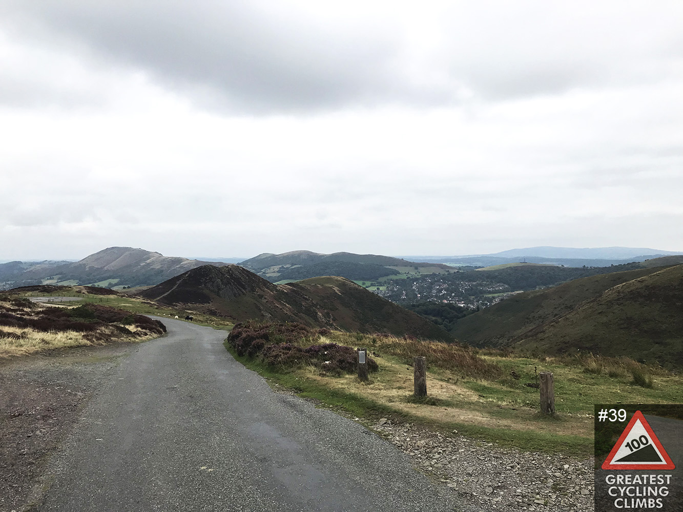 Cycling The Burway - winding road with hillsides and grey sky, 100 Greatest Cycling Climbs logo