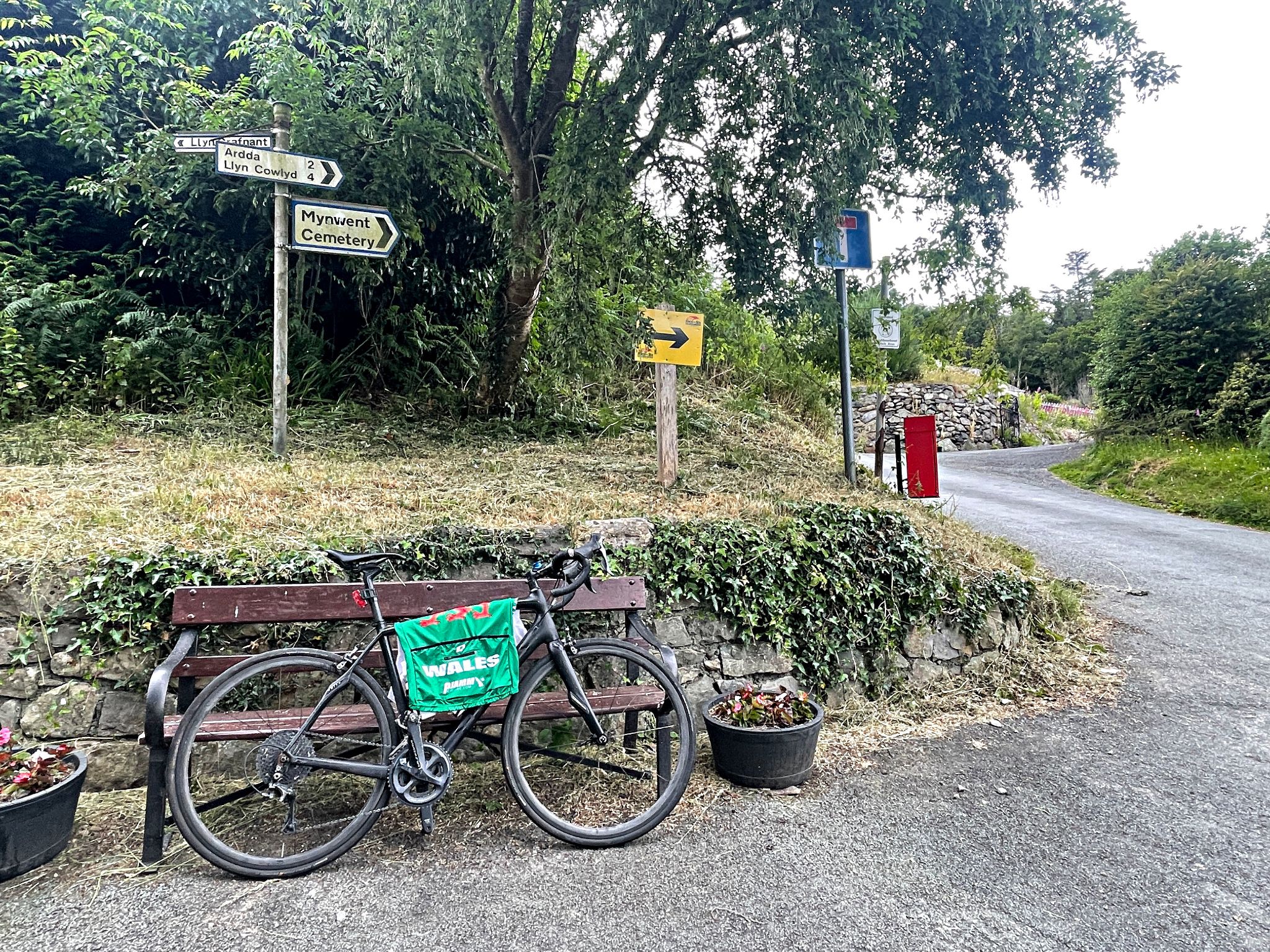bike parked against bench in front of street signs for Mynwent Cemetery, Ardda, and Llyn Cowlyd