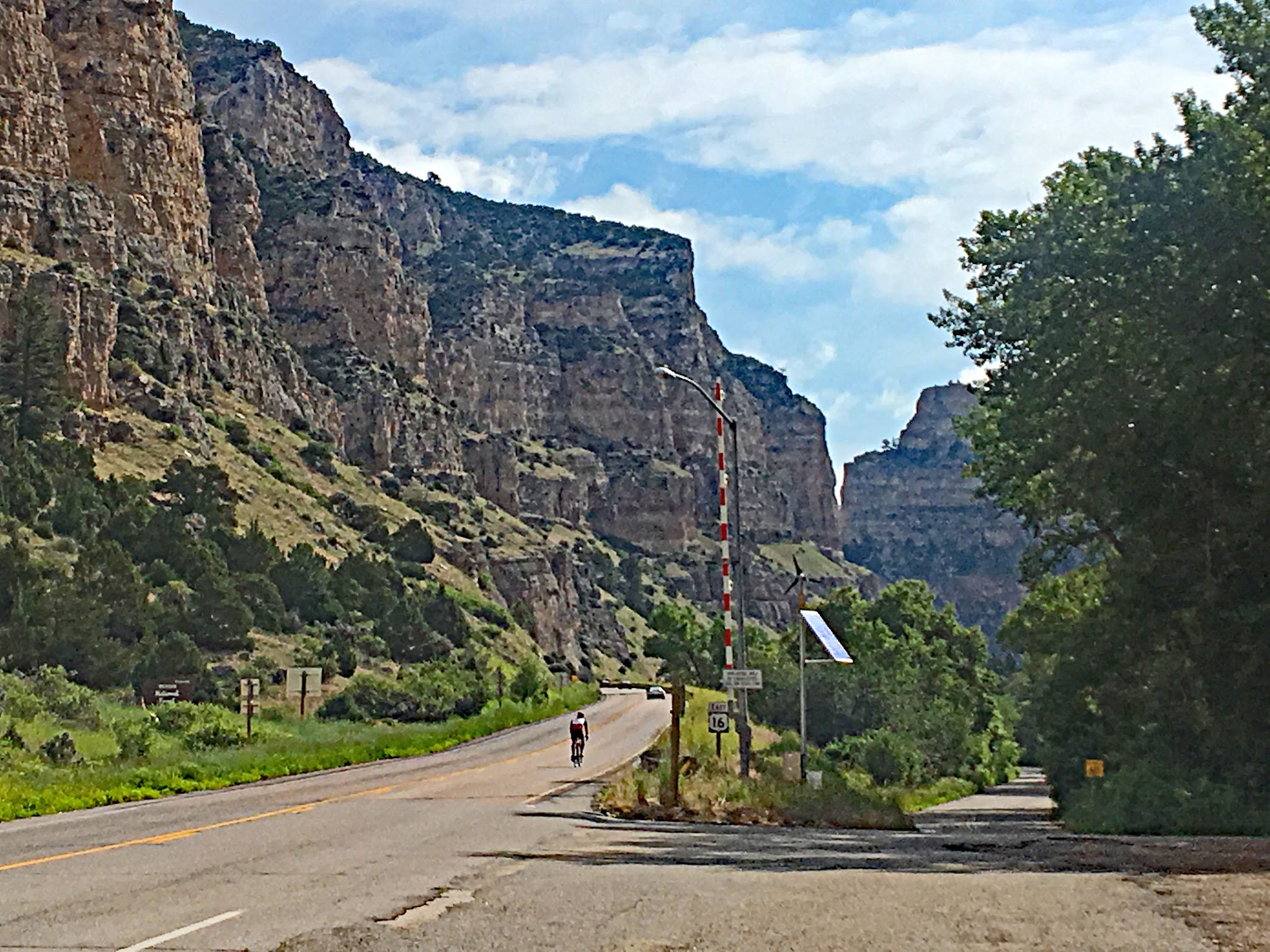 Cycling Powder River, Wyoming - cyclist rides in the distance on straight stretch of road surrounded by tall rock formations