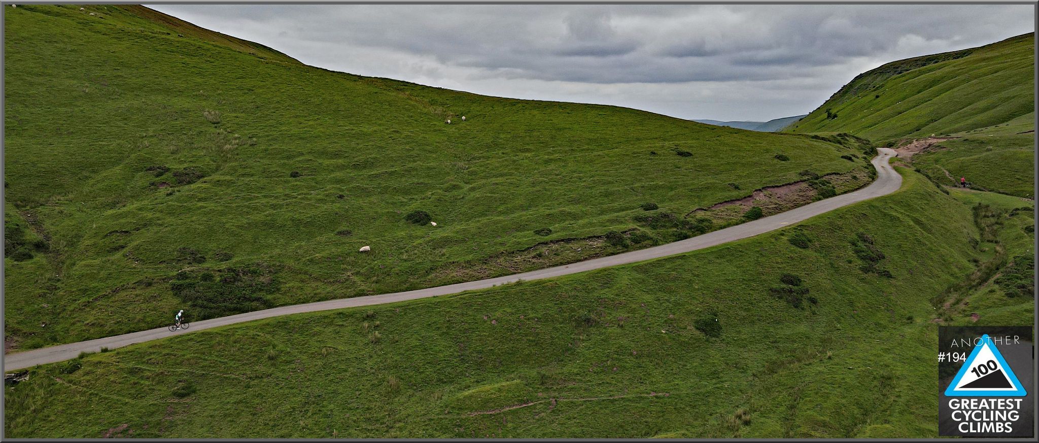 Cycling Gospel Pass North, Wales panoramic aerial view shows long stretch of roadway in green hillside, PJAMM Cyclist climbing on road
