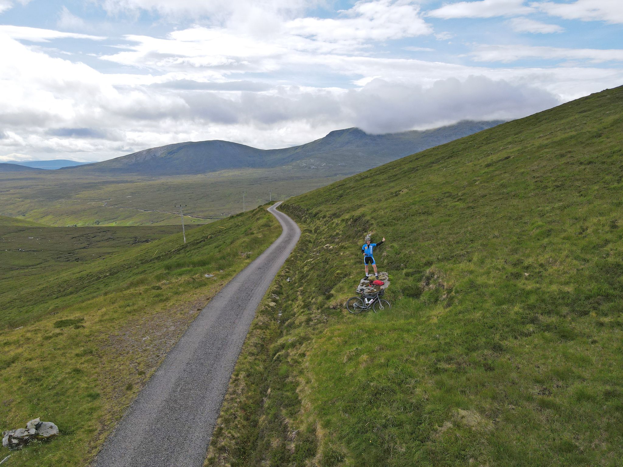 PJAMM Cyclist stands with bike on rock in pasture next to road side at climb finish