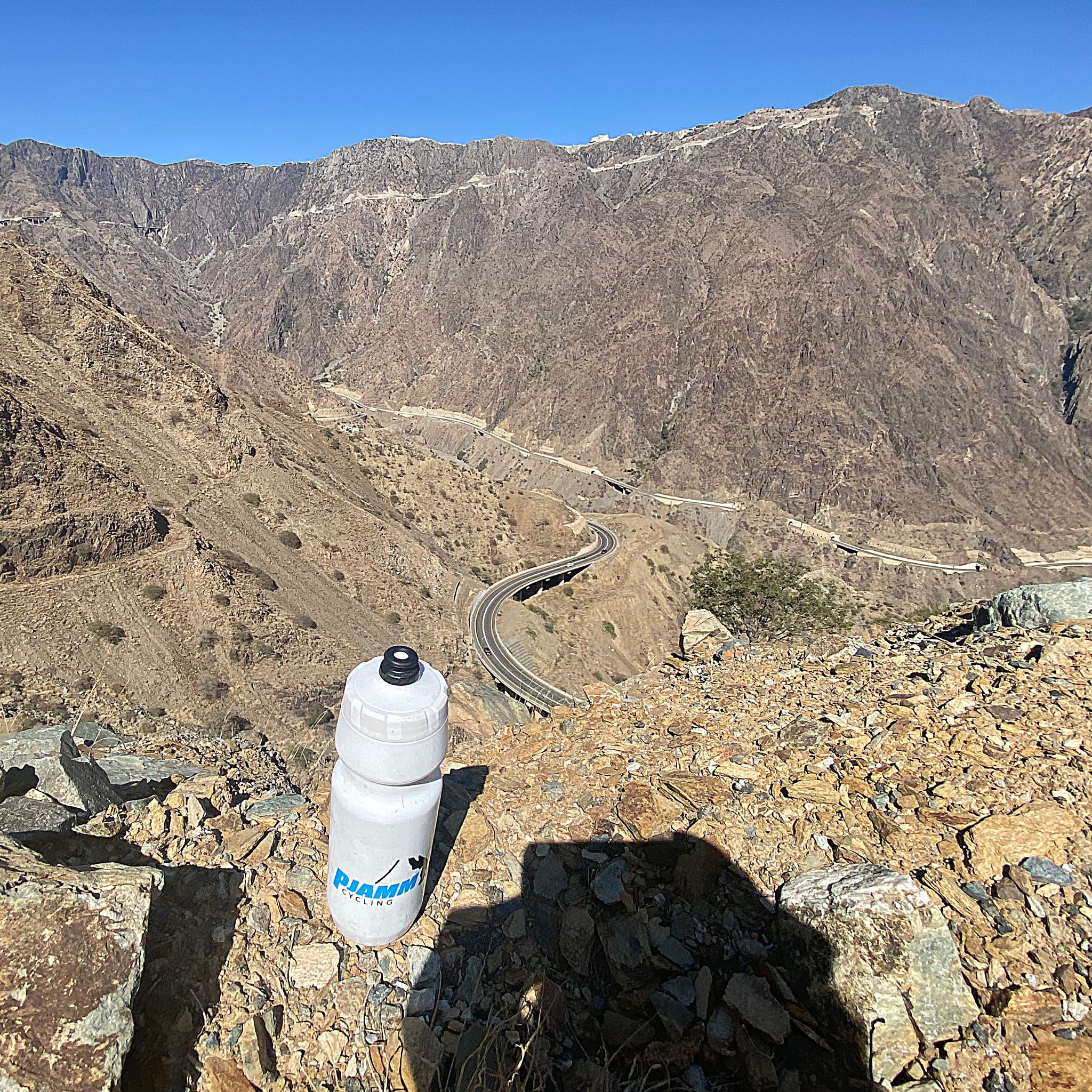 PJAMM Cycling water bottle sits on mountainside looking down at roadway carved in mountains far below