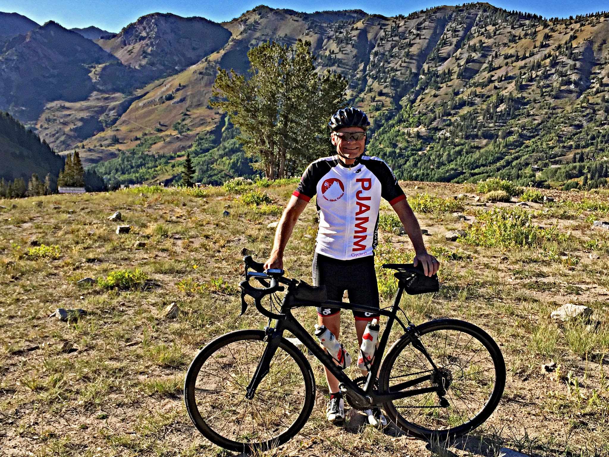 Cyclist with bike at top of Little Cottonwood Canyon climb by bike.