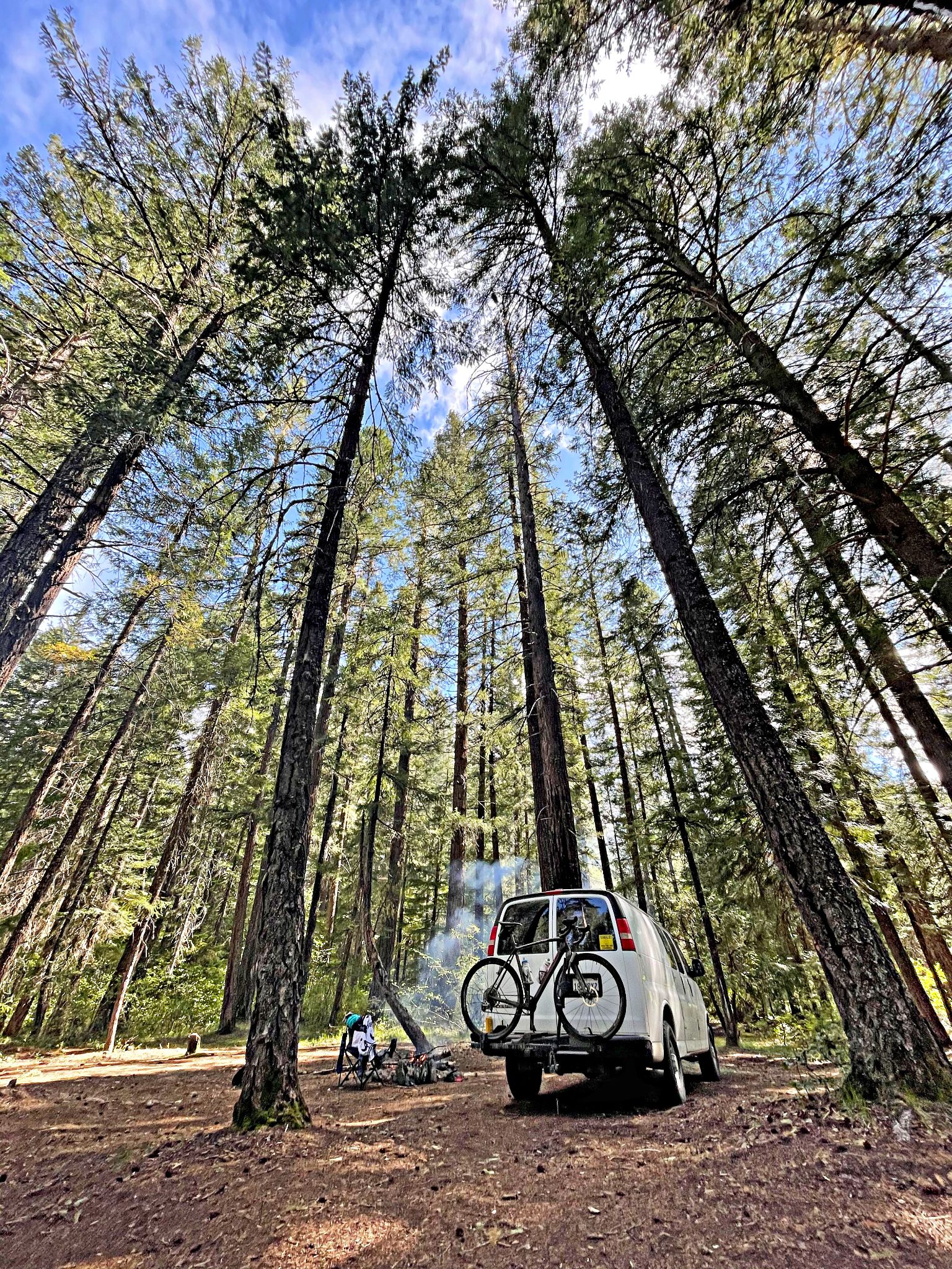 Camping at Mazama Campground; tall evergreen trees surround white camping van with bikes on back
