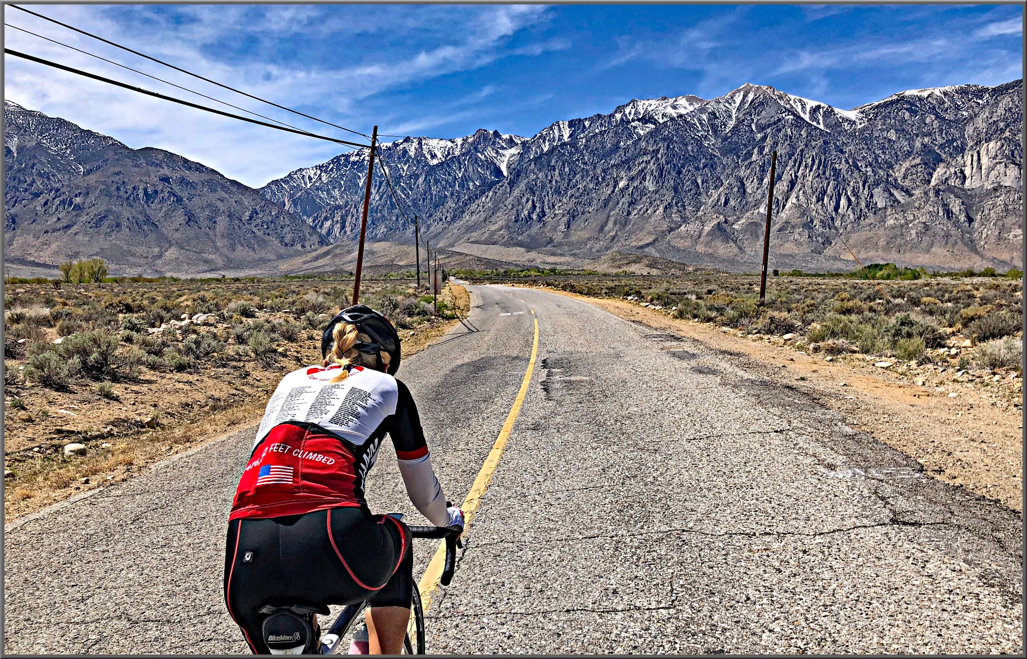 Cycling Pine Creek Road, California - PJAMM Cyclist rides on two-lane highway road in high desert setting, mountains in front of her