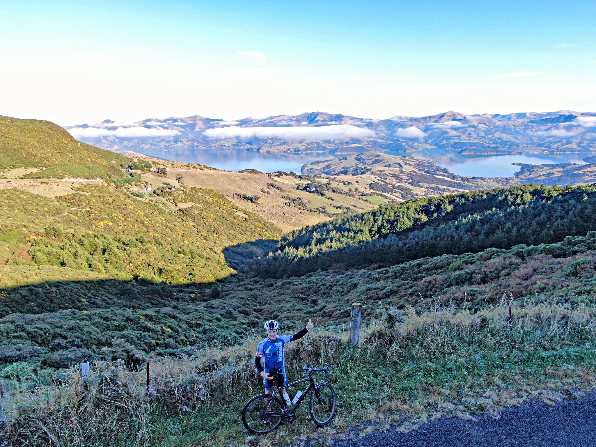 PJAMM Cycling's Brad Butterfield stands at climb summit with bike, giving thumbs up