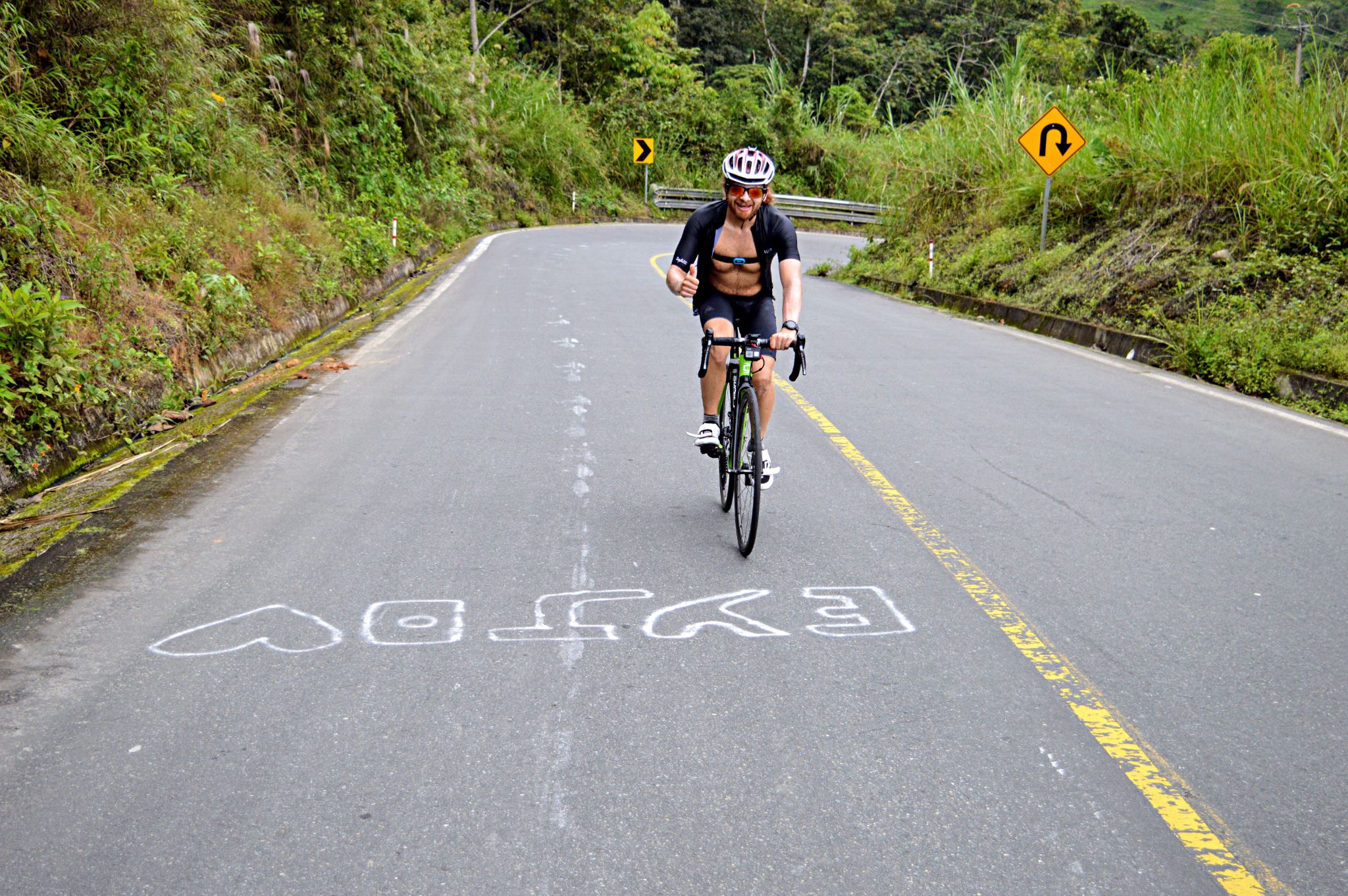 PJAMM Cyclist Hernando smiles and gives a thumbs up on his bike while cycling on two-lane mountain roadway on El Torneado climb