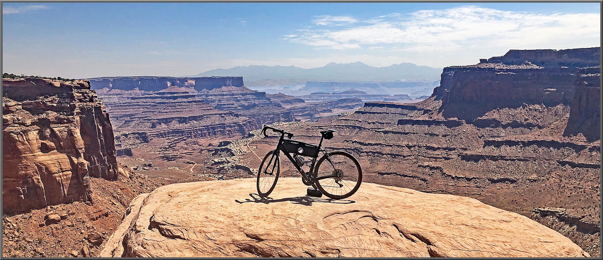 Cycling Shafer Trail, Canyonlands National Park - bike sitting atop flat rock plateau overlooking  brown canyons and blue mountains far in the distance