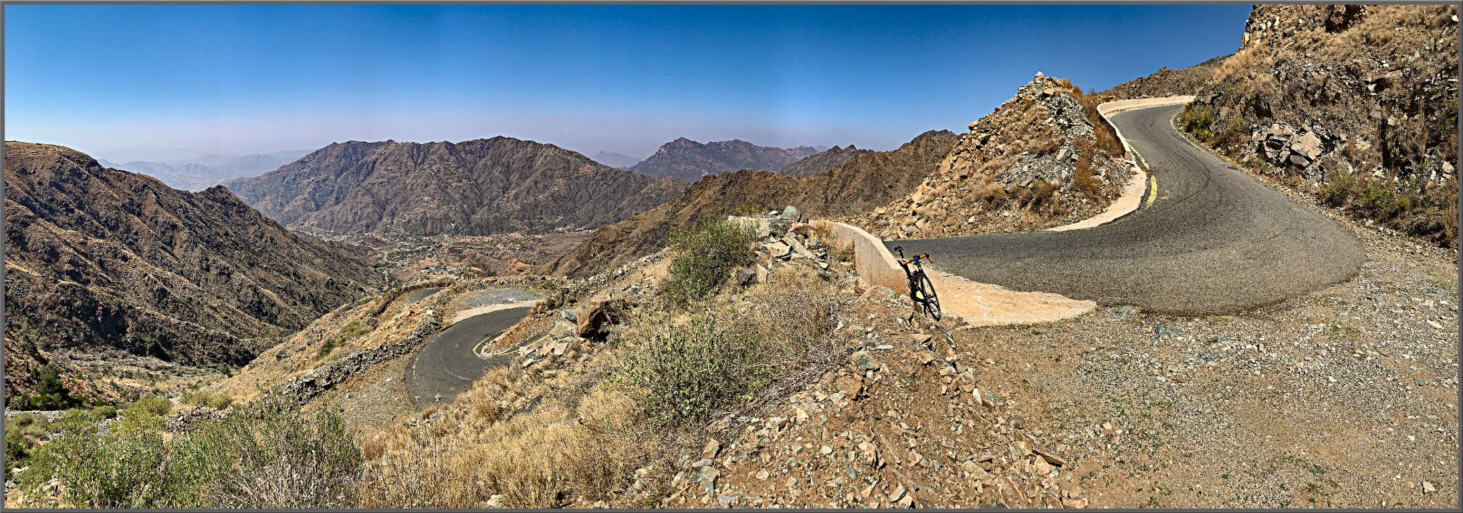 Al Jaada Pass, Asir Mountains, Saudi Arabia - panoramic view shows bike learning against guardrail on side of road at hairpin turn in mountain roadway