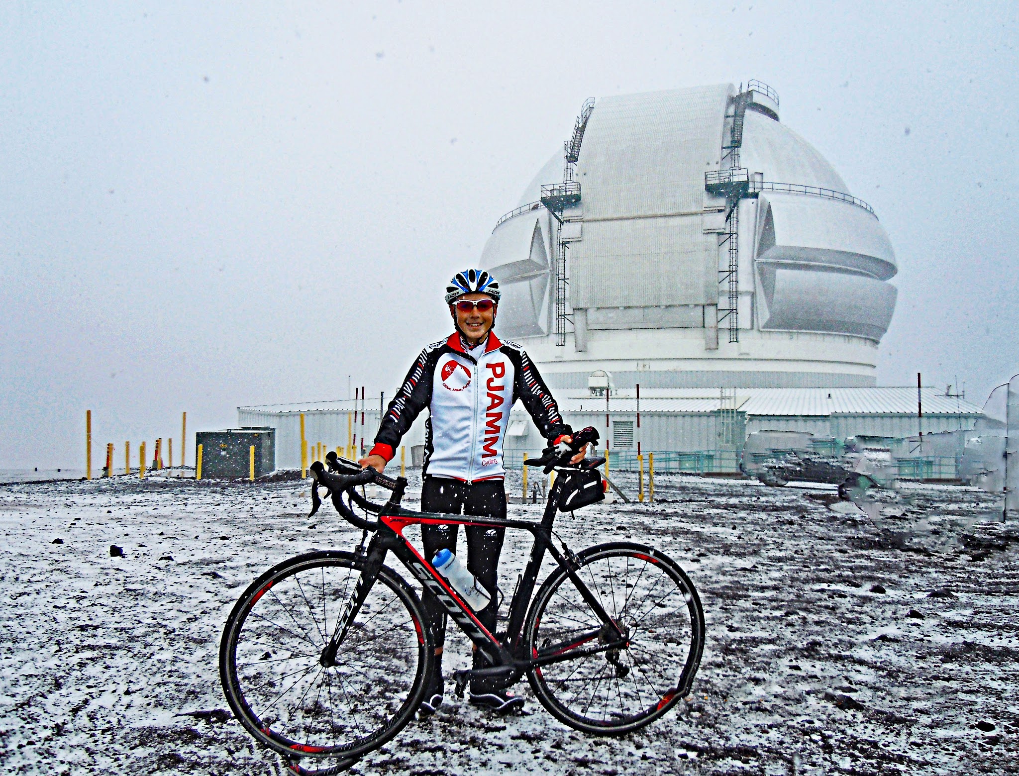 PJAMM Cyclist stands with bike at observation center at summit of Mauna Kea climb, in full snow