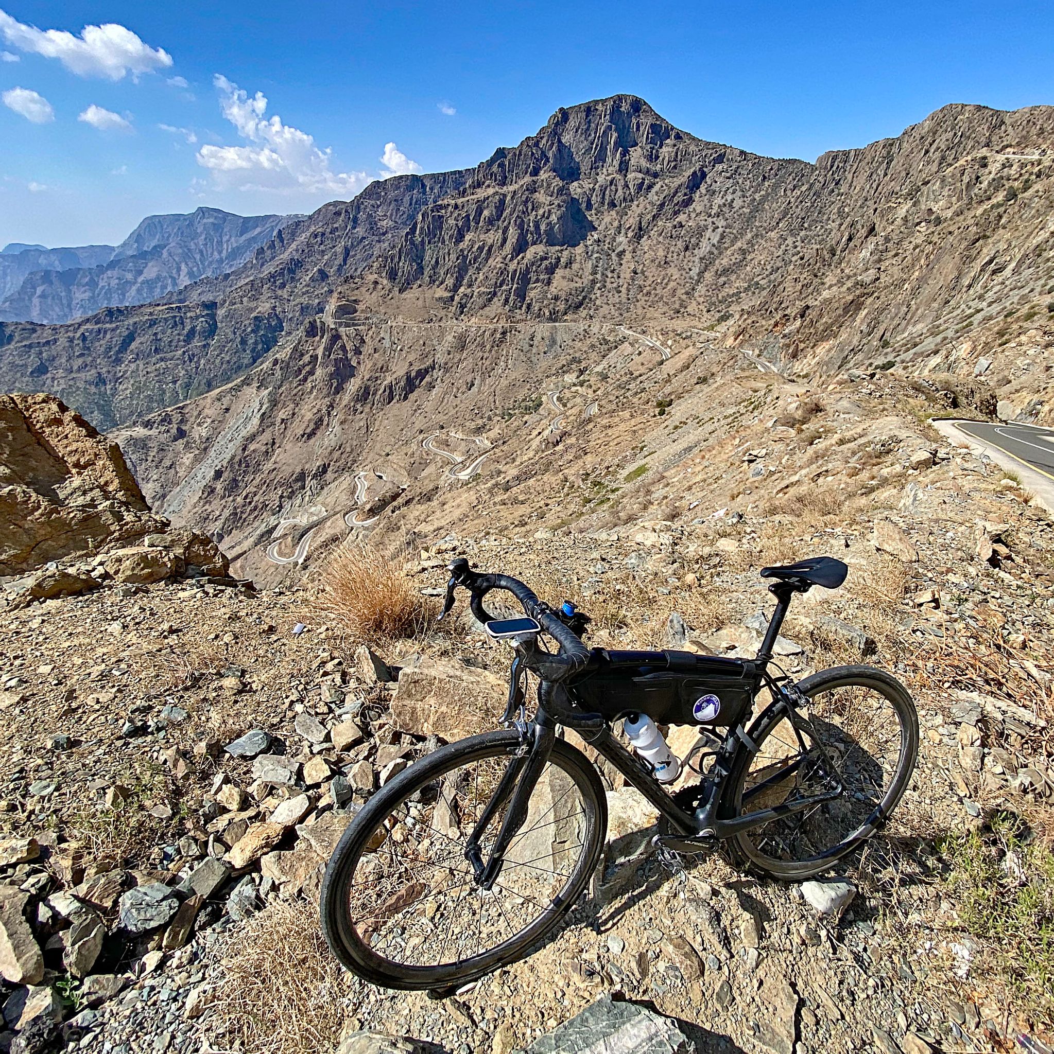 Cycling Bani Horairah - bike parked in rocky terrain on side of road, hairpin turns can be seen in distance center of photo